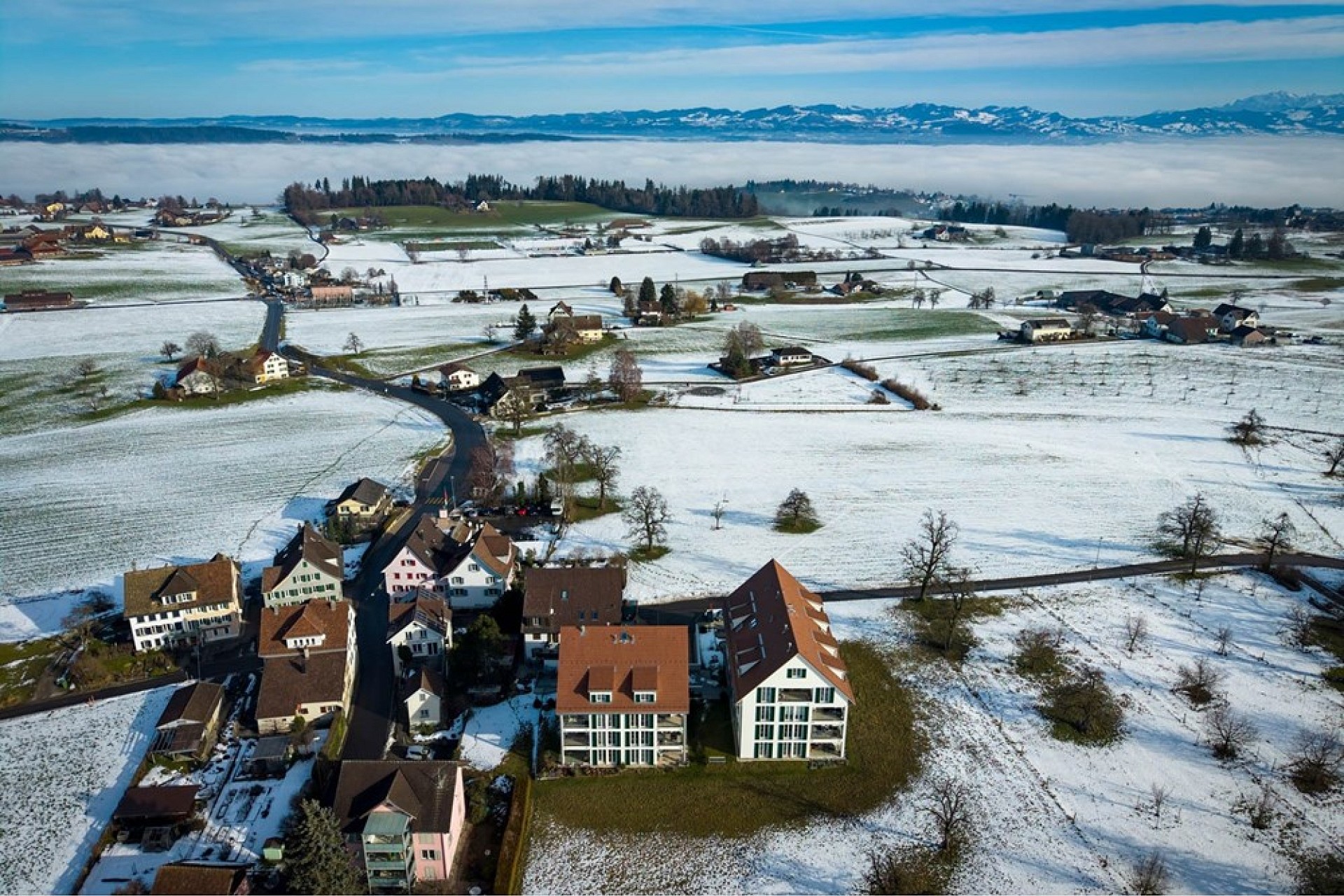 Luftaufnahme eines verschneiten Dorfes mit Alpenblick
