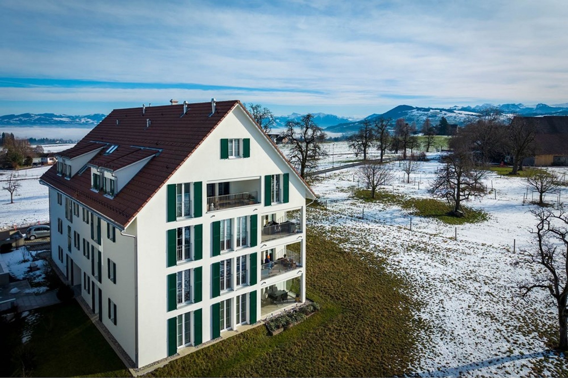 Luftaufnahme eines Einfamilienhauses im Schnee mit Alpenblick