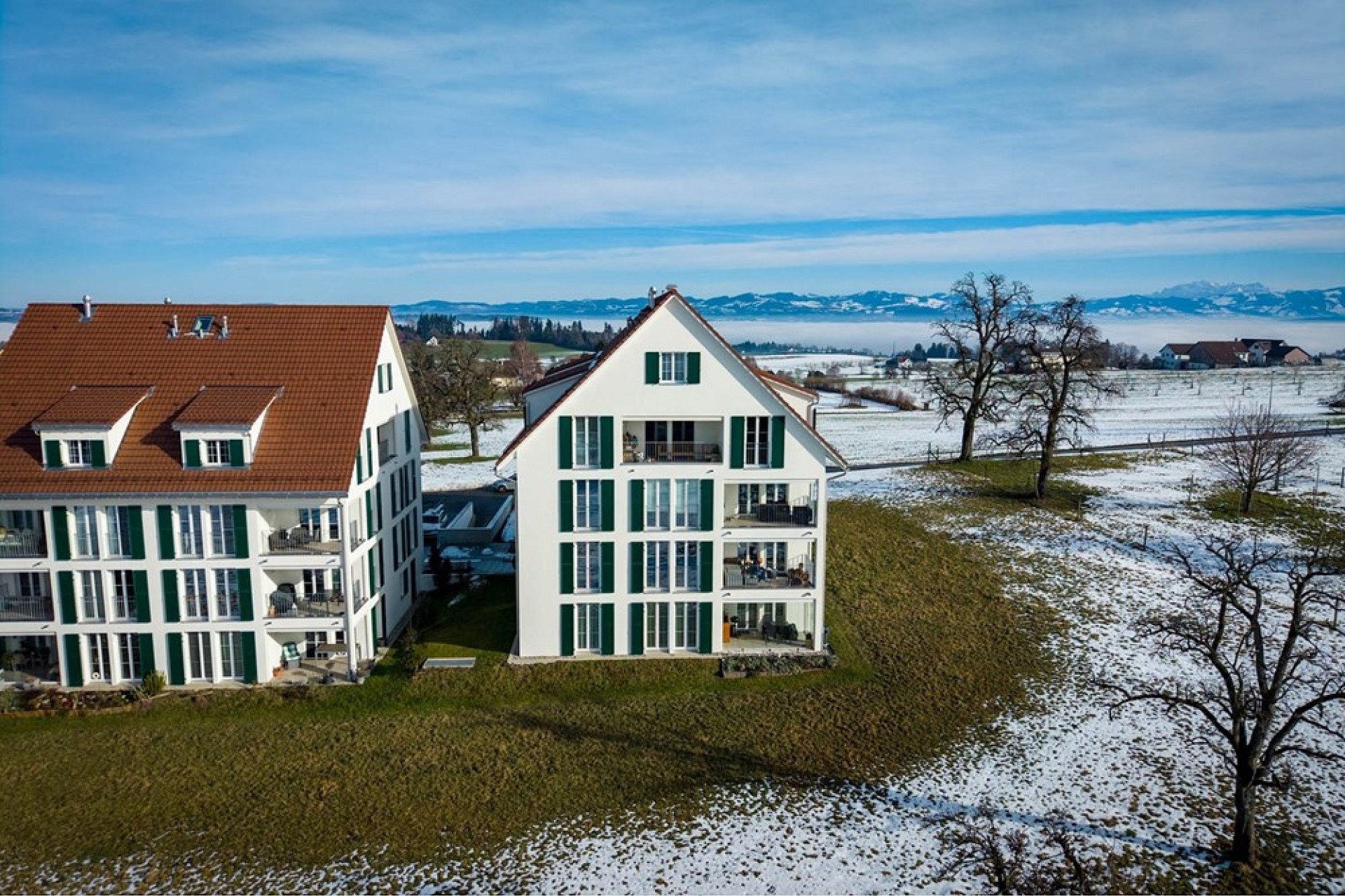 Luftaufnahme von zwei Wohngebäuden mit Blick auf Schnee, Felder und Alpenpanorama