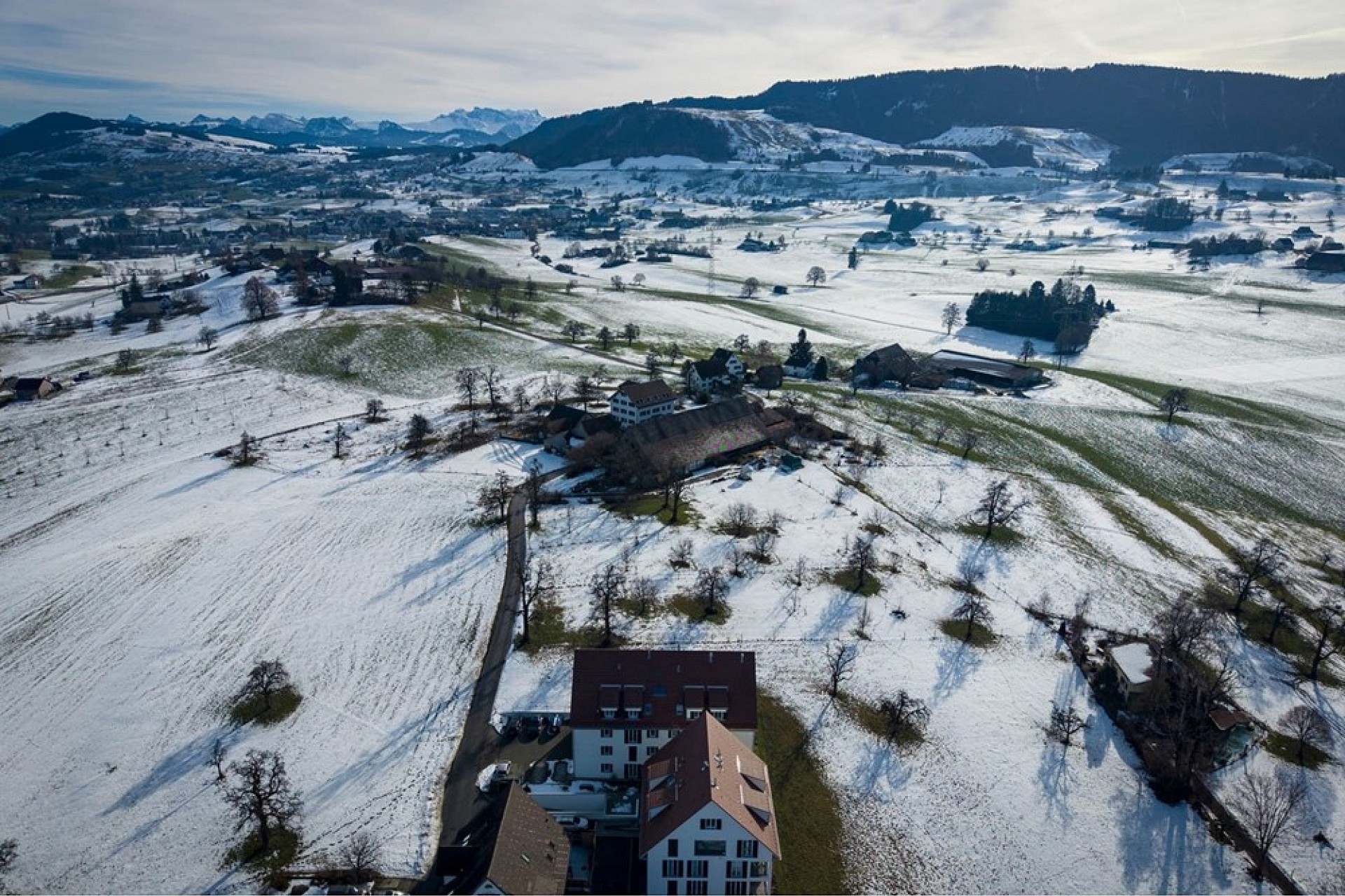 Luftaufnahme einer verschneiten Alpenlandschaft mit Gebäuden