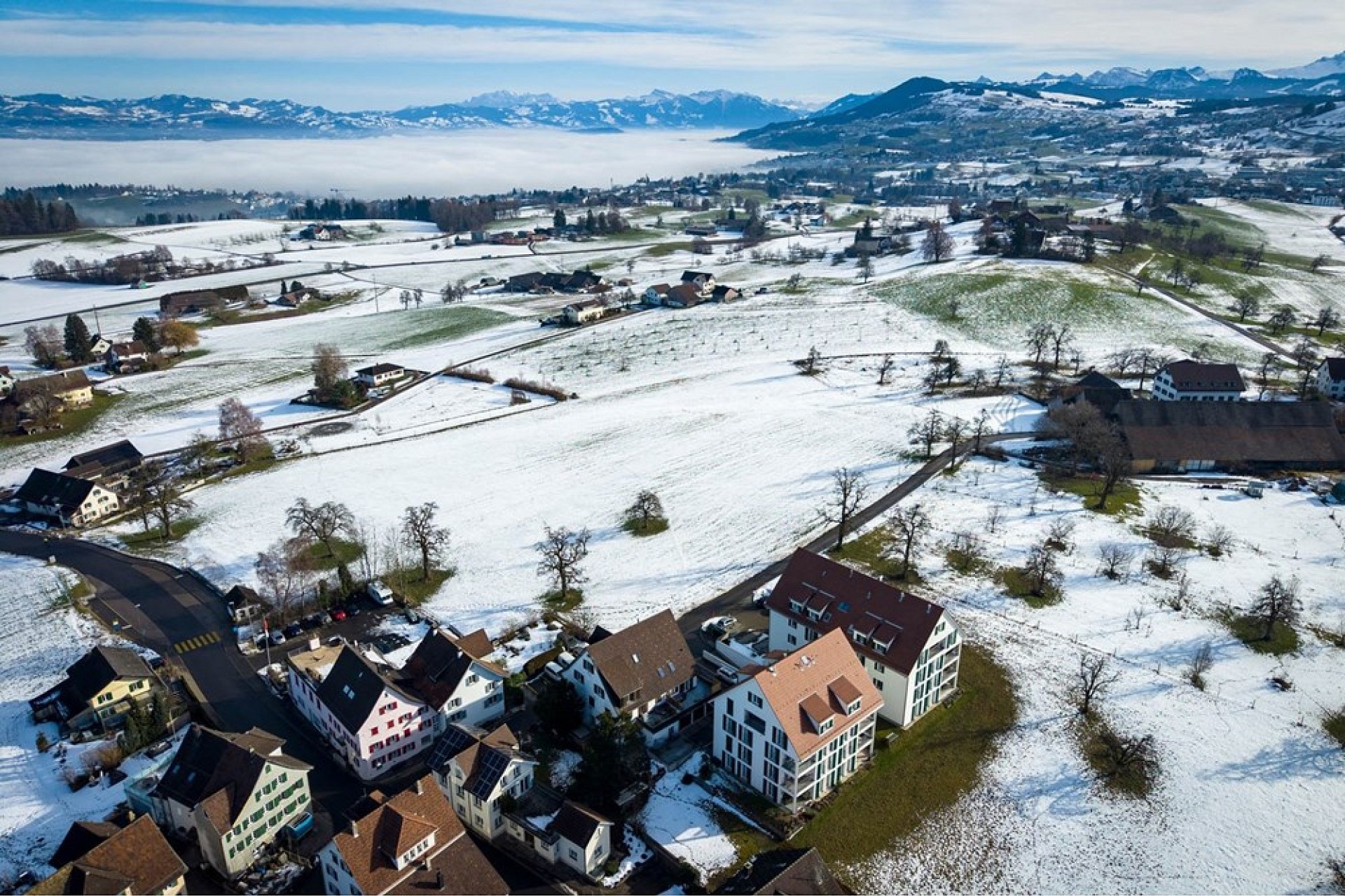 Luftaufnahme einer verschneiten Landschaft mit Blick auf See und Berge