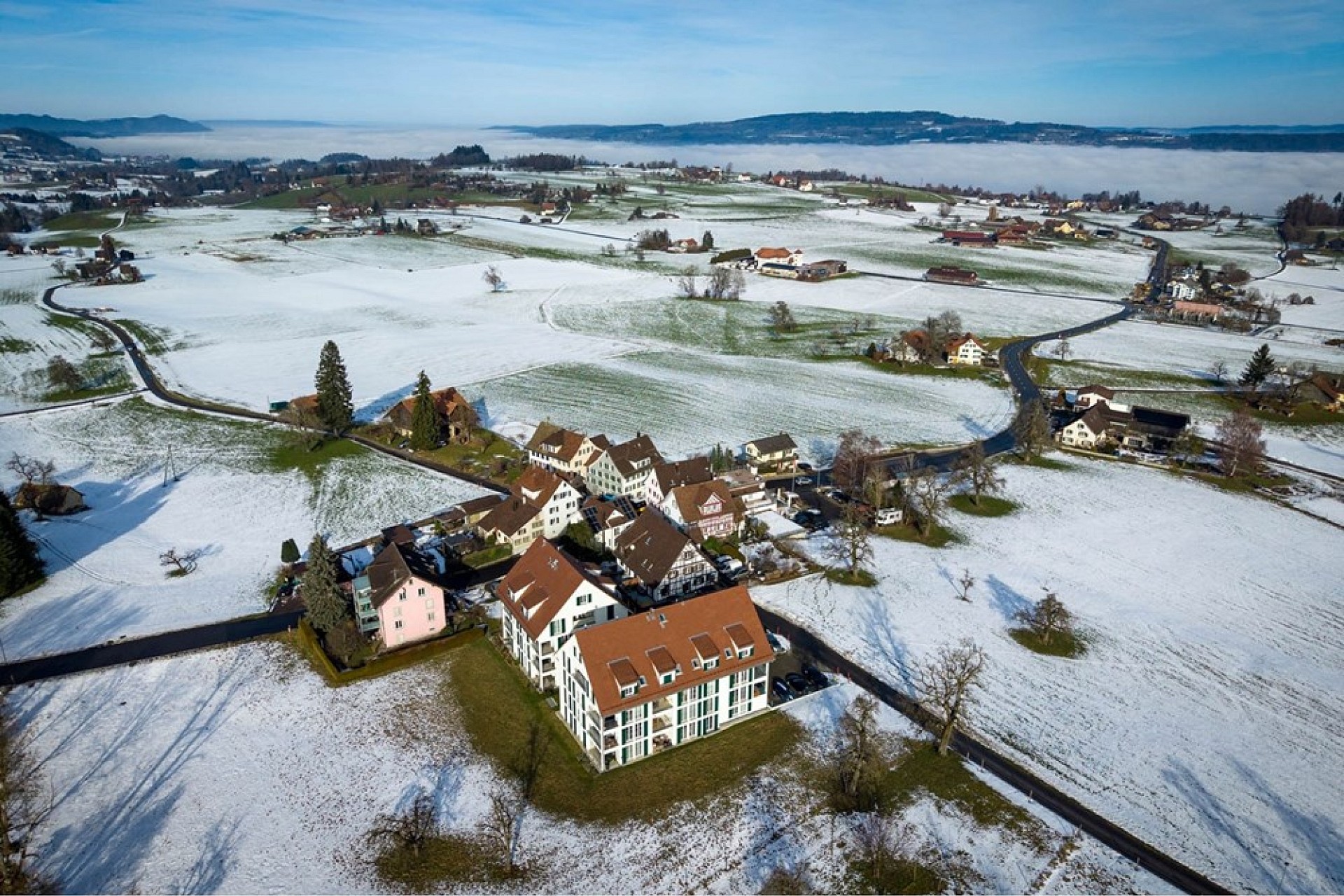 Luftaufnahme eines verschneiten ländlichen Siedlungsgebiets am See