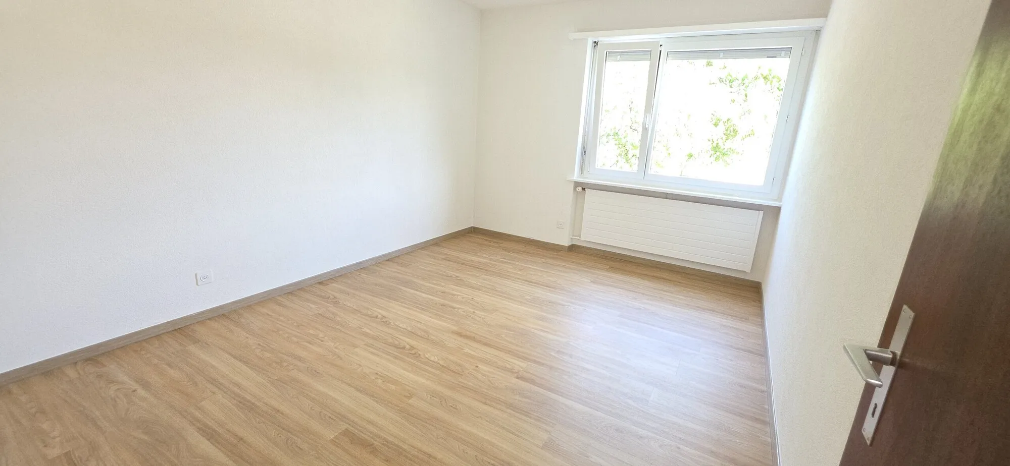 Leeres, helles Zimmer mit Holzoptik-Boden