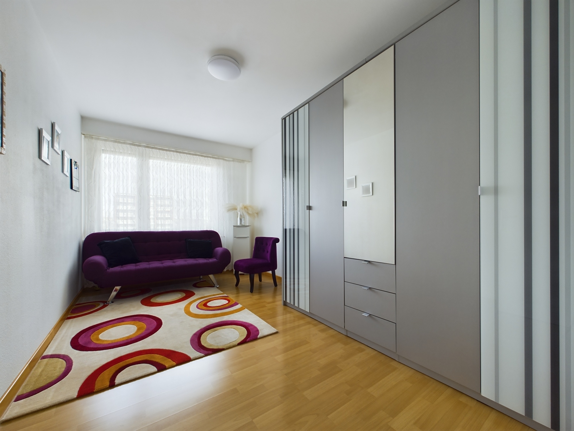 Helles Schlafzimmer mit violetter Sitzgruppe und großem Kleiderschrank