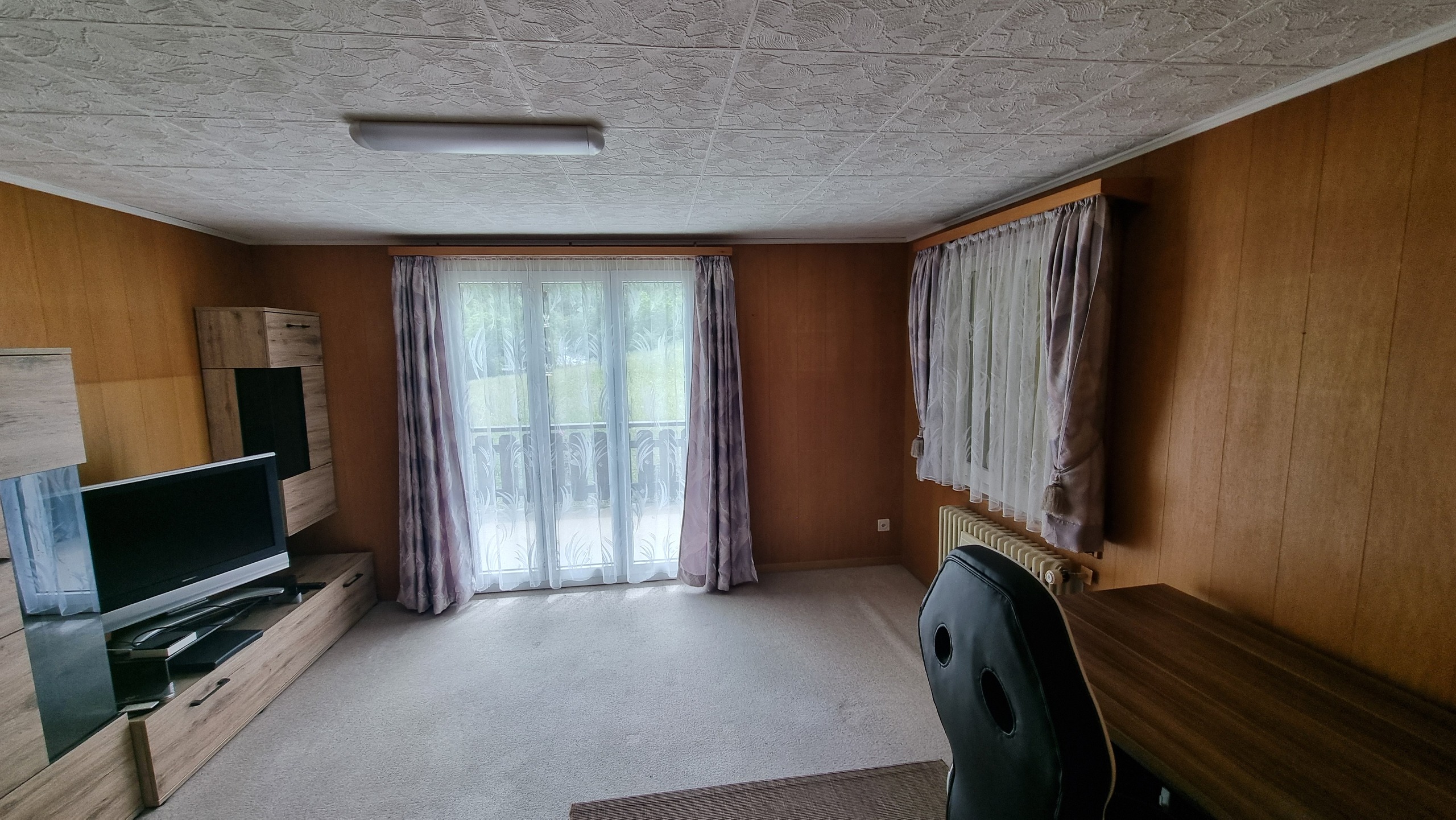 Wohnzimmer mit Holzvertäfelung und Balkonfenstern