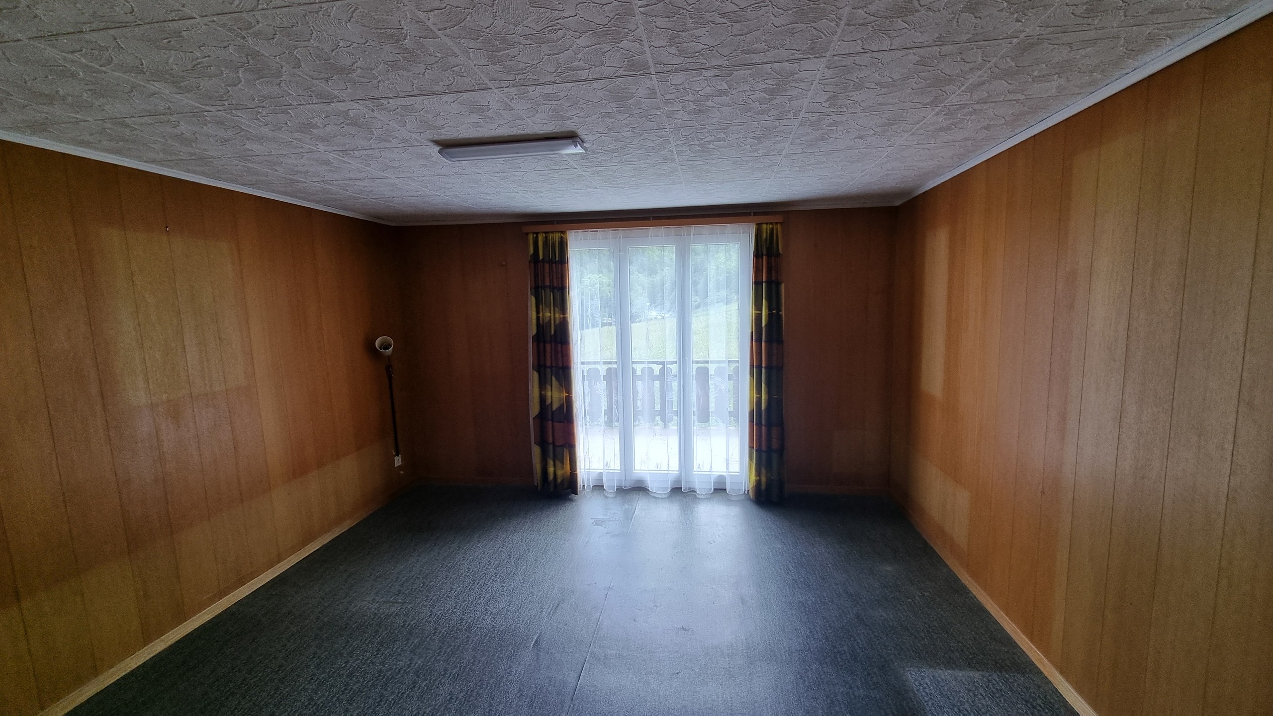 Leerer Wohnraum mit Holzvertäfelung und Balkontür