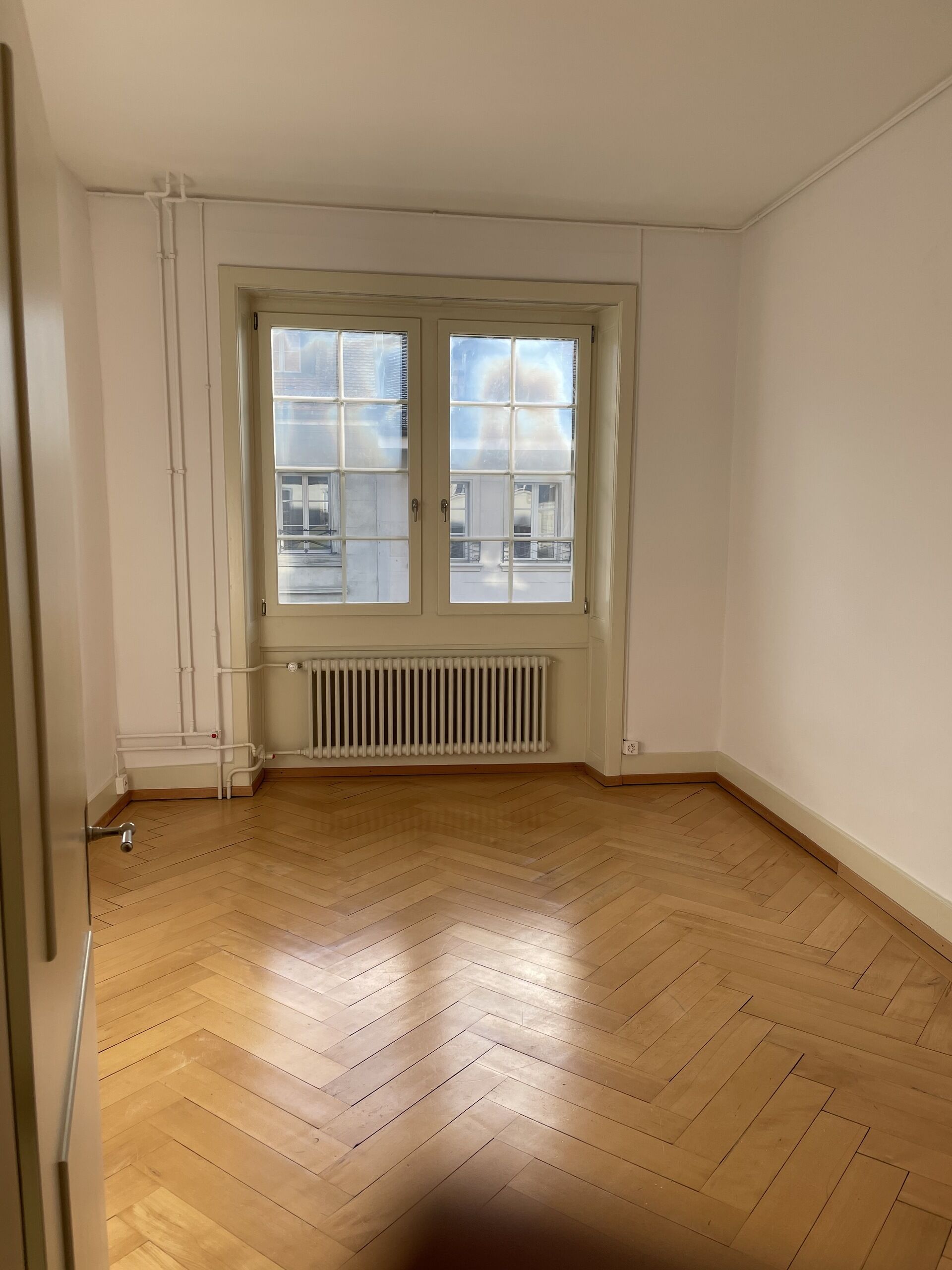 Leerer Altbau-Raum mit Fischgrätparkett und Fenster