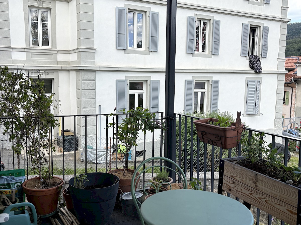 Balkon mit Pflanzen vor einem hellen Wohnhaus
