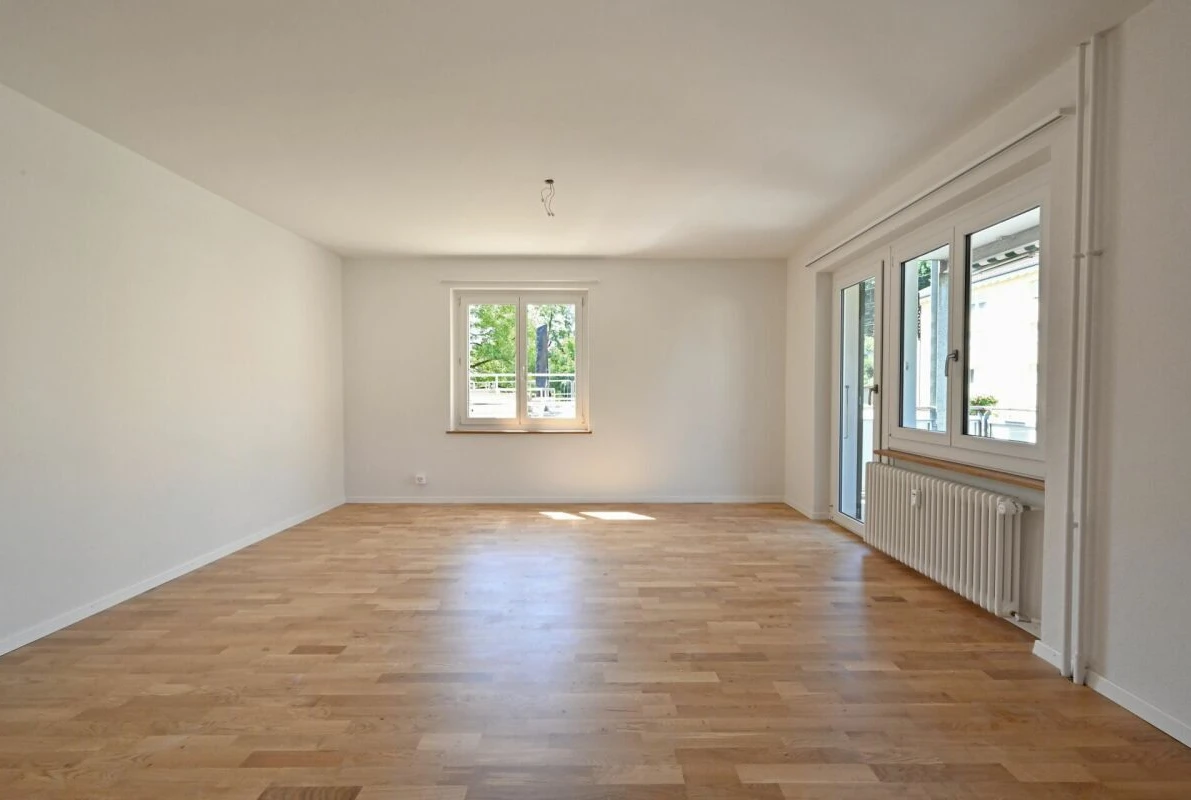 Heller leerer Wohnraum mit Parkettboden und großen Fenstern