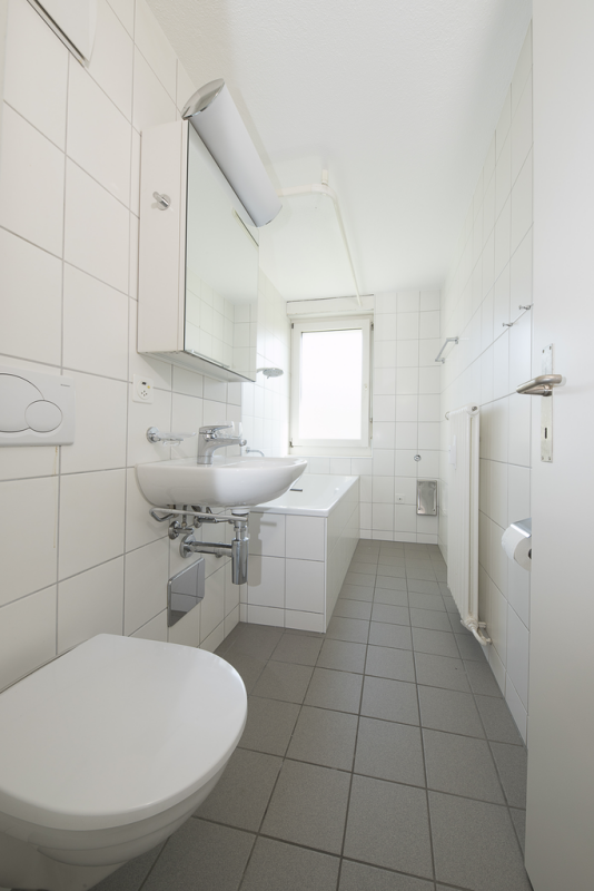 Schmales, weiß gefliestes Badezimmer mit Badewanne und Waschtisch