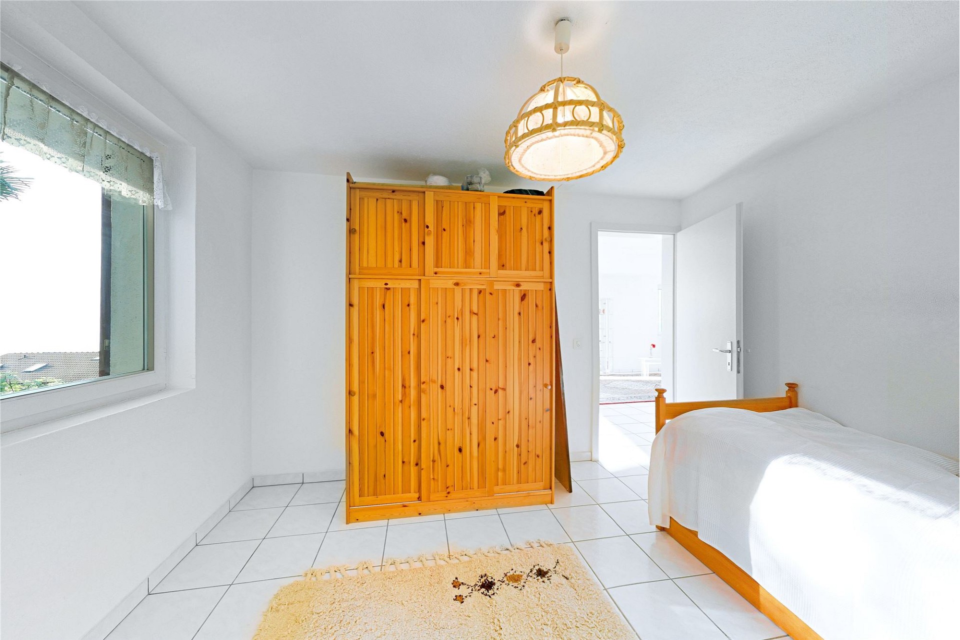 Helles Schlafzimmer mit Fliesenboden und Holzschrank