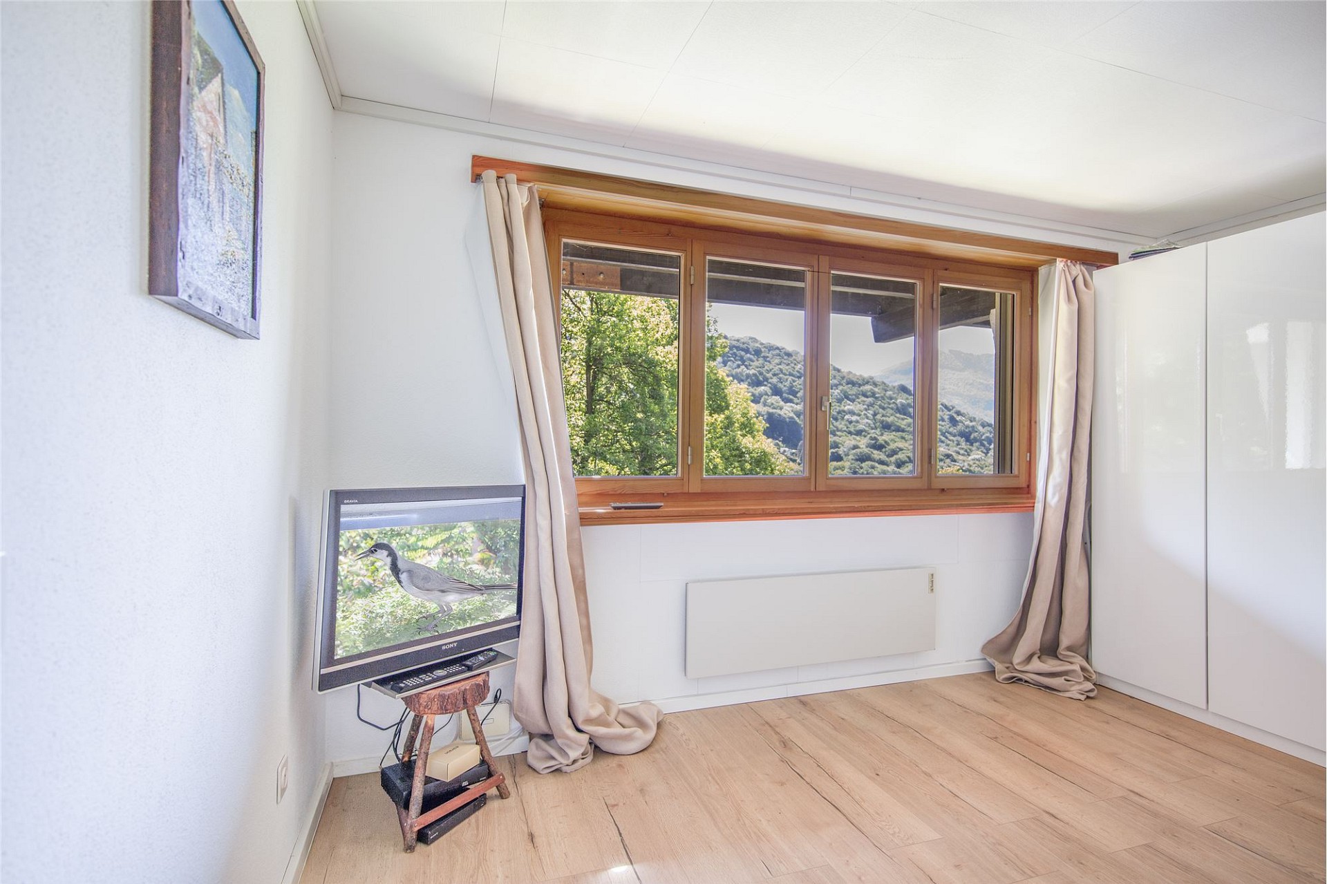Hell eingerichtetes Zimmer mit großem Holzfenster und Bergblick