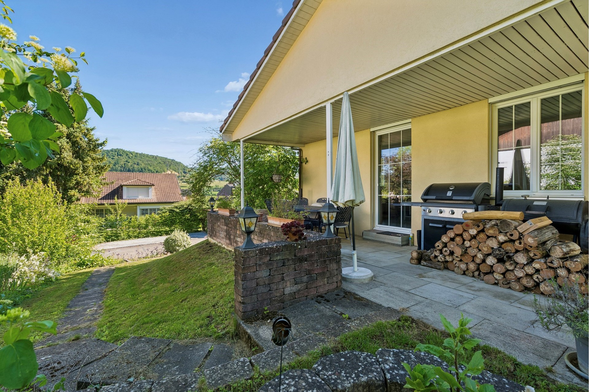 Überdachte Terrasse mit Grill und Gartenblick