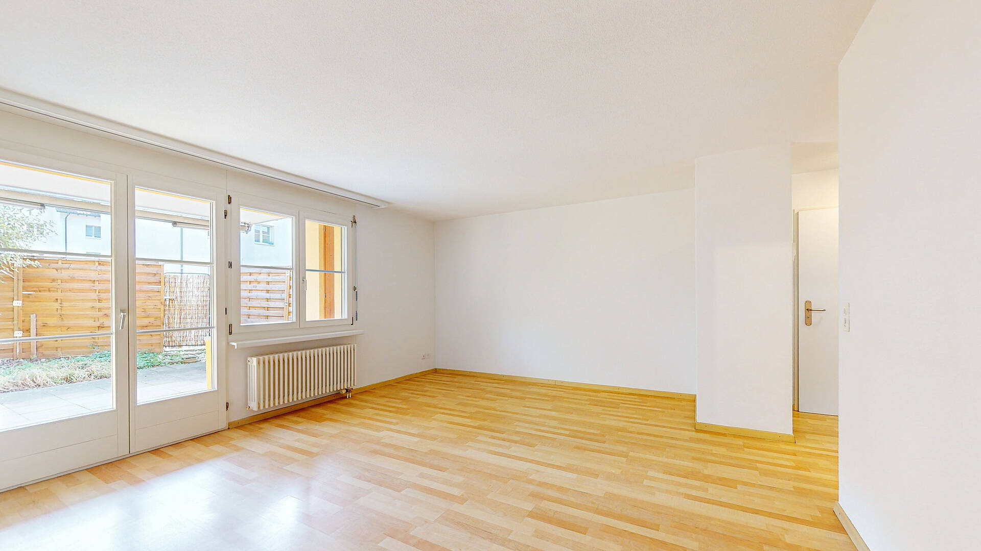 Helles, leeres Wohn-/Aufenthaltszimmer mit Parkett und Terrassentür