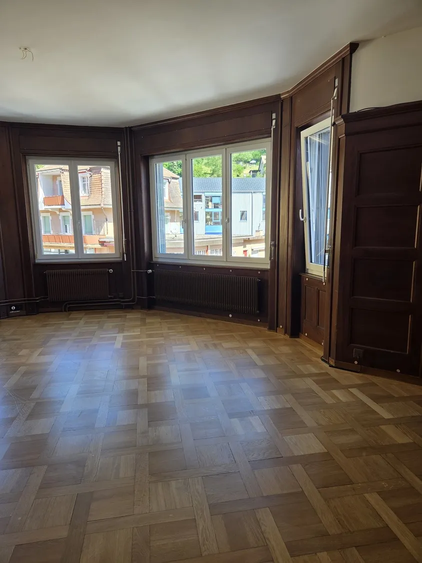 Heller Wohnraum mit Erkerfenstern und Parkettboden