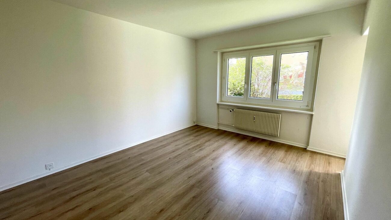 Leerer heller Raum mit Holzoptikboden und Fenster