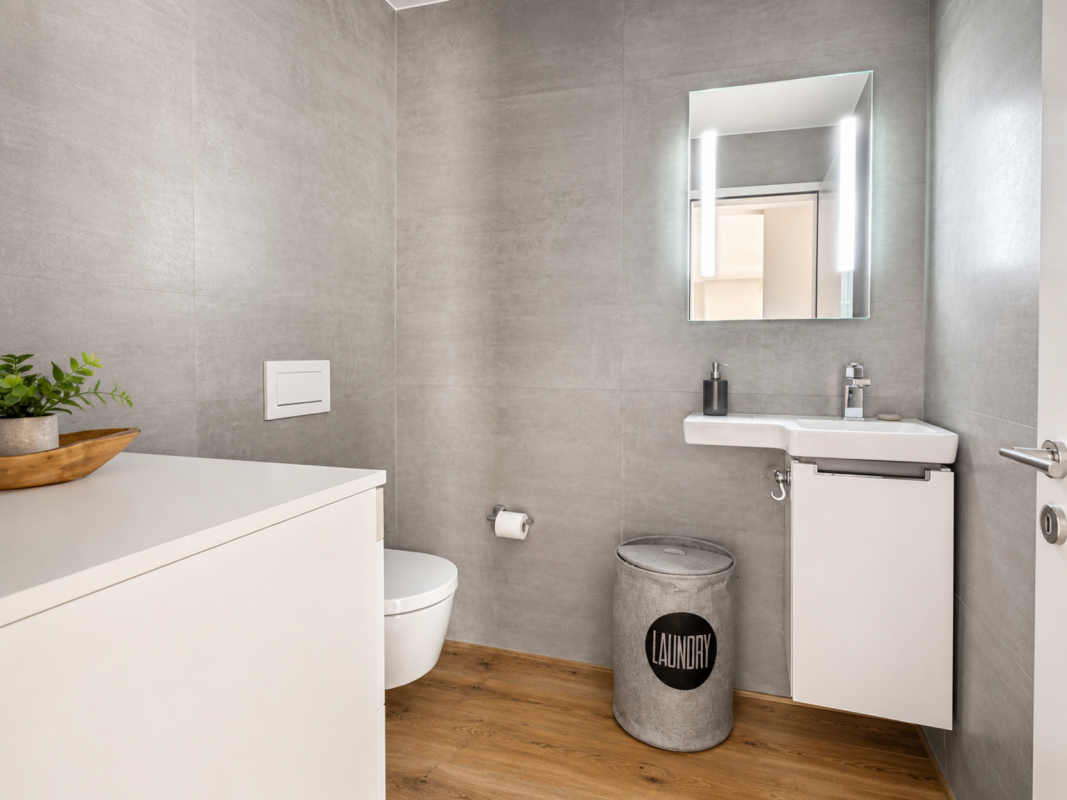 Modernes Gäste-WC mit grauen Wandfliesen und Holzoptikboden