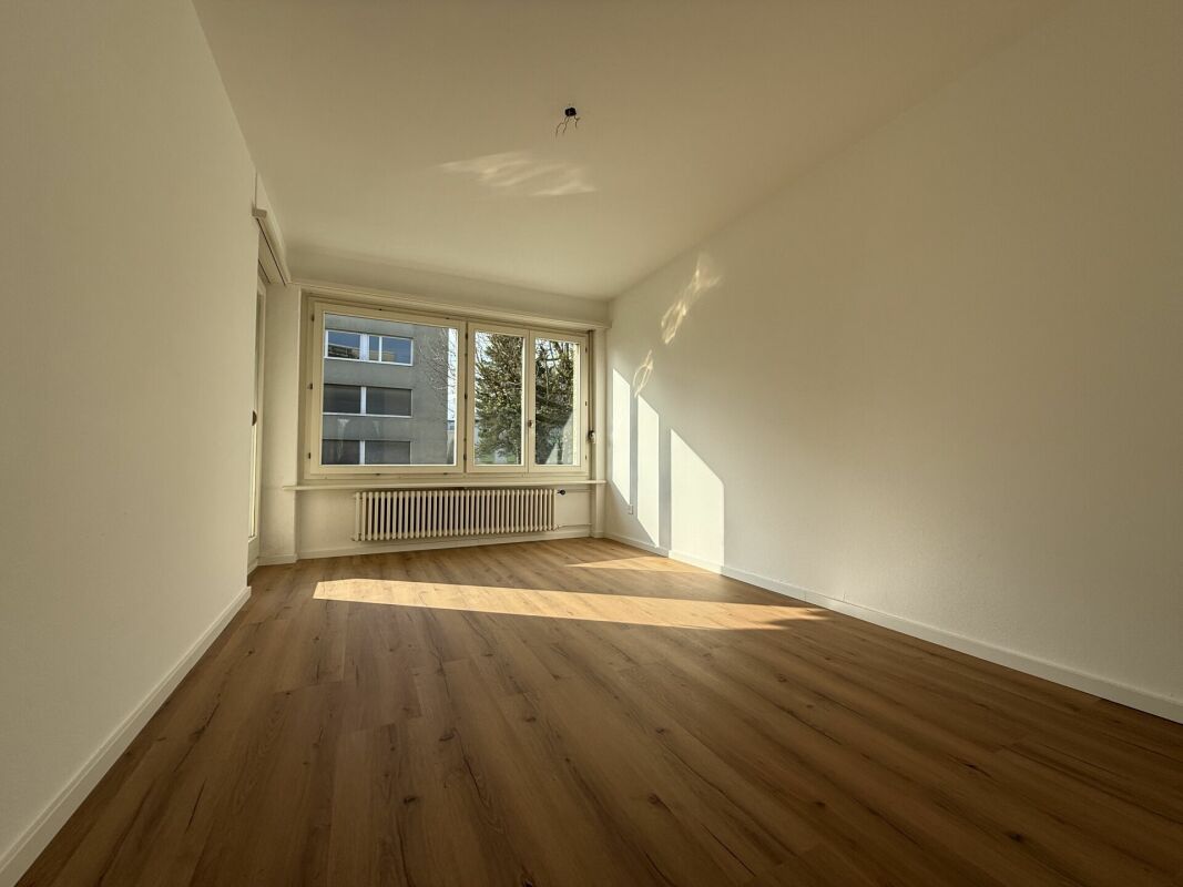 Heller leerer Raum mit Parkett und großem Fenster