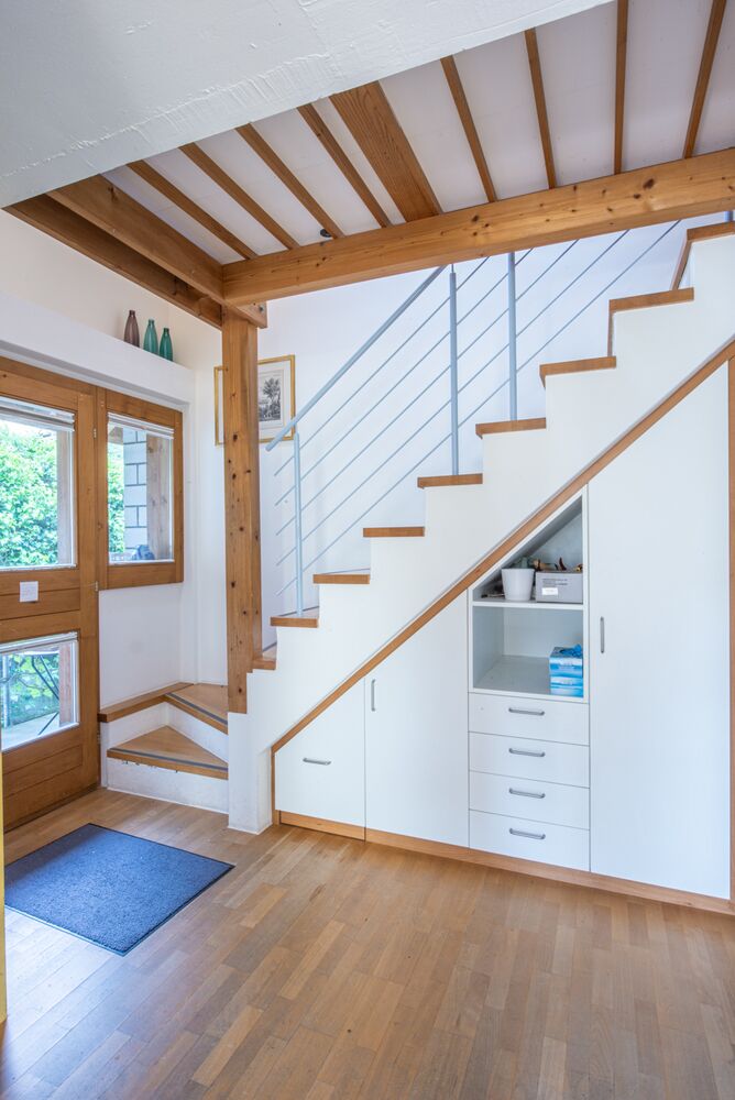 Heller Eingangsbereich mit Holztreppe und Stauraum unter der Treppe