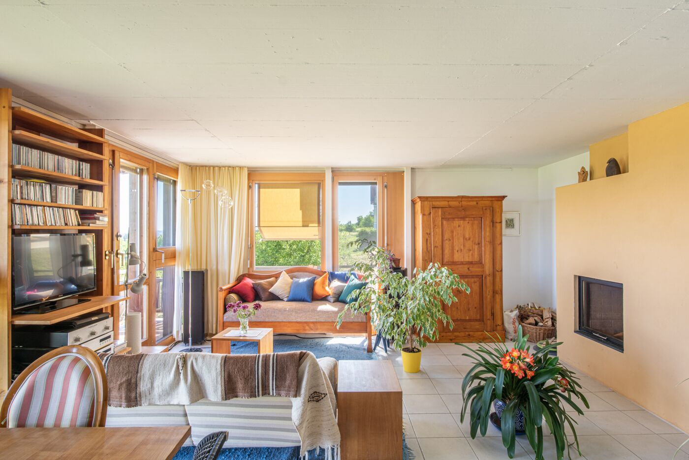 Wohnzimmer mit Kamin, Bücherregal und großen Fenstern
