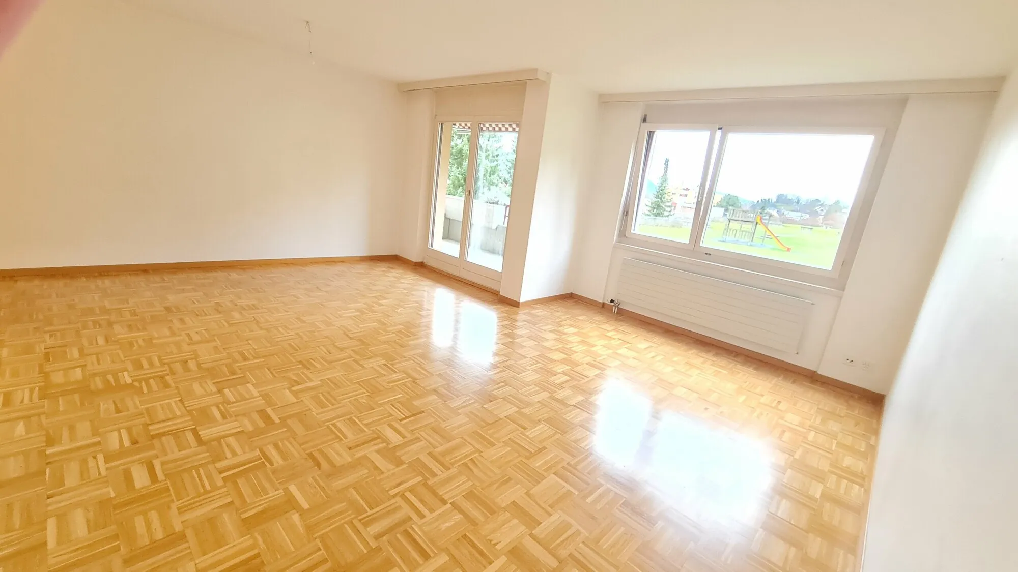 Heller leerer Wohnraum mit Parkettboden und großen Fenstern