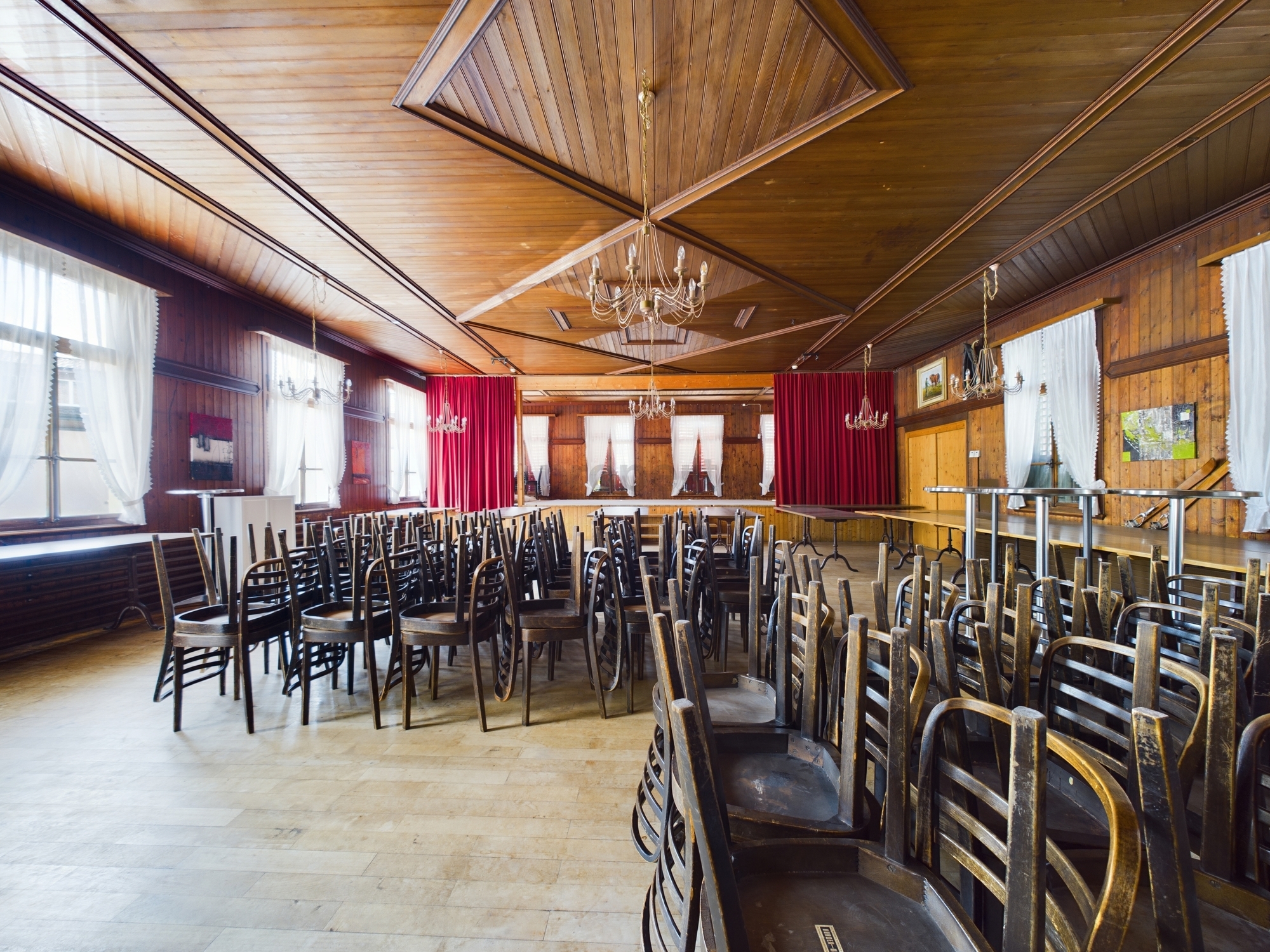 Großer holzvertäfelter Saal mit gestapelten Stühlen
