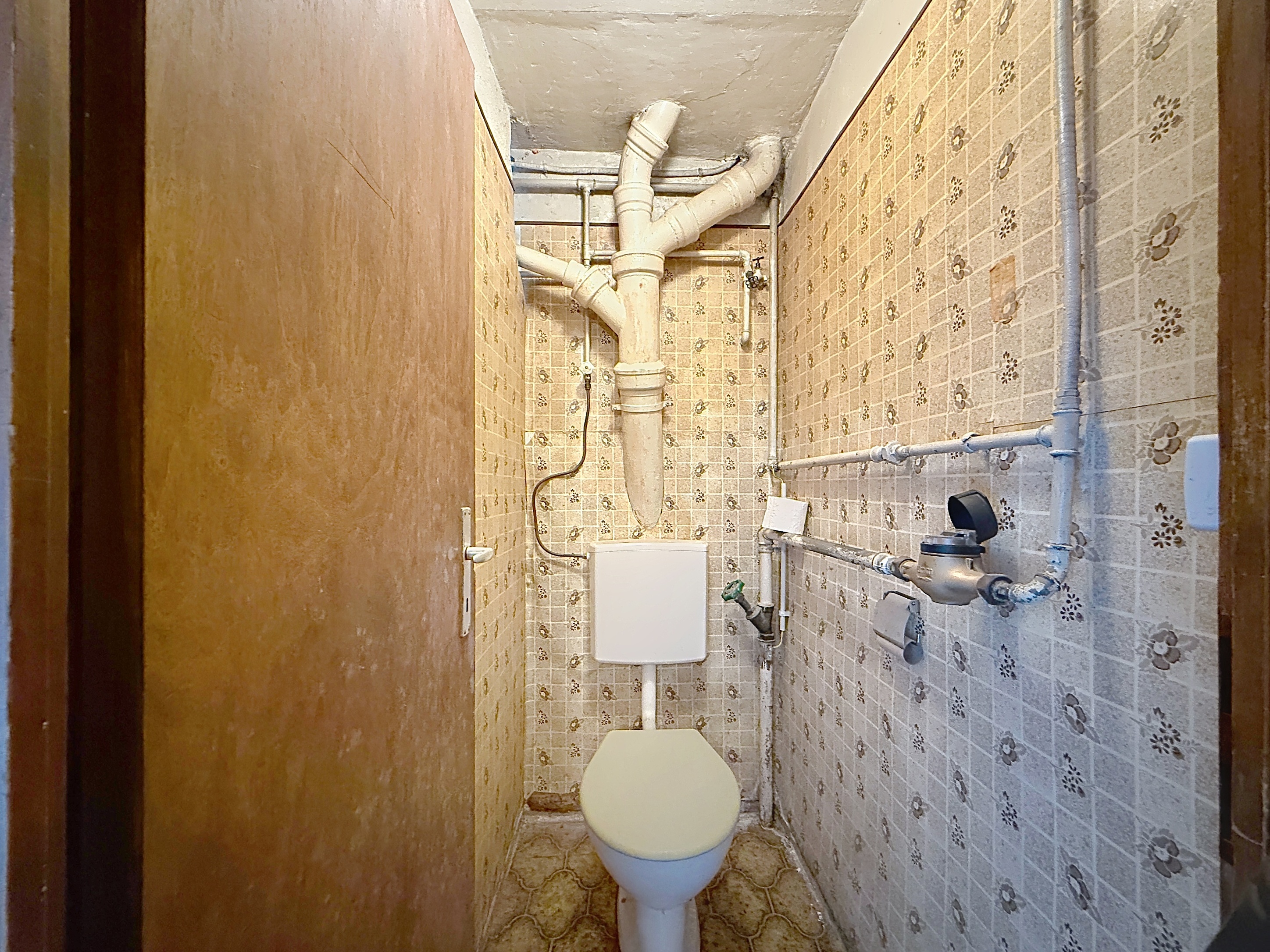 Kleines WC mit sichtbaren Rohrleitungen