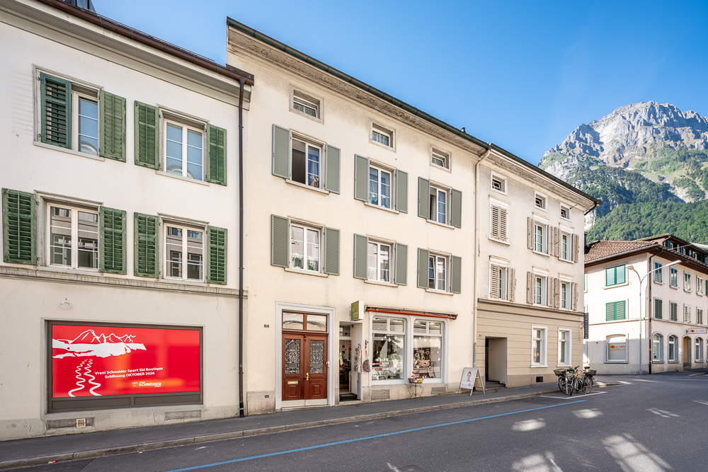 Straßenansicht mit historischen Wohn- und Geschäftshäusern vor Bergkulisse