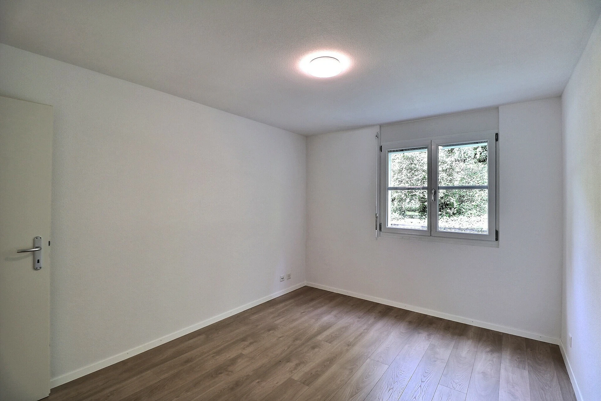 Helles, leeres Zimmer mit Fenster und Holzboden