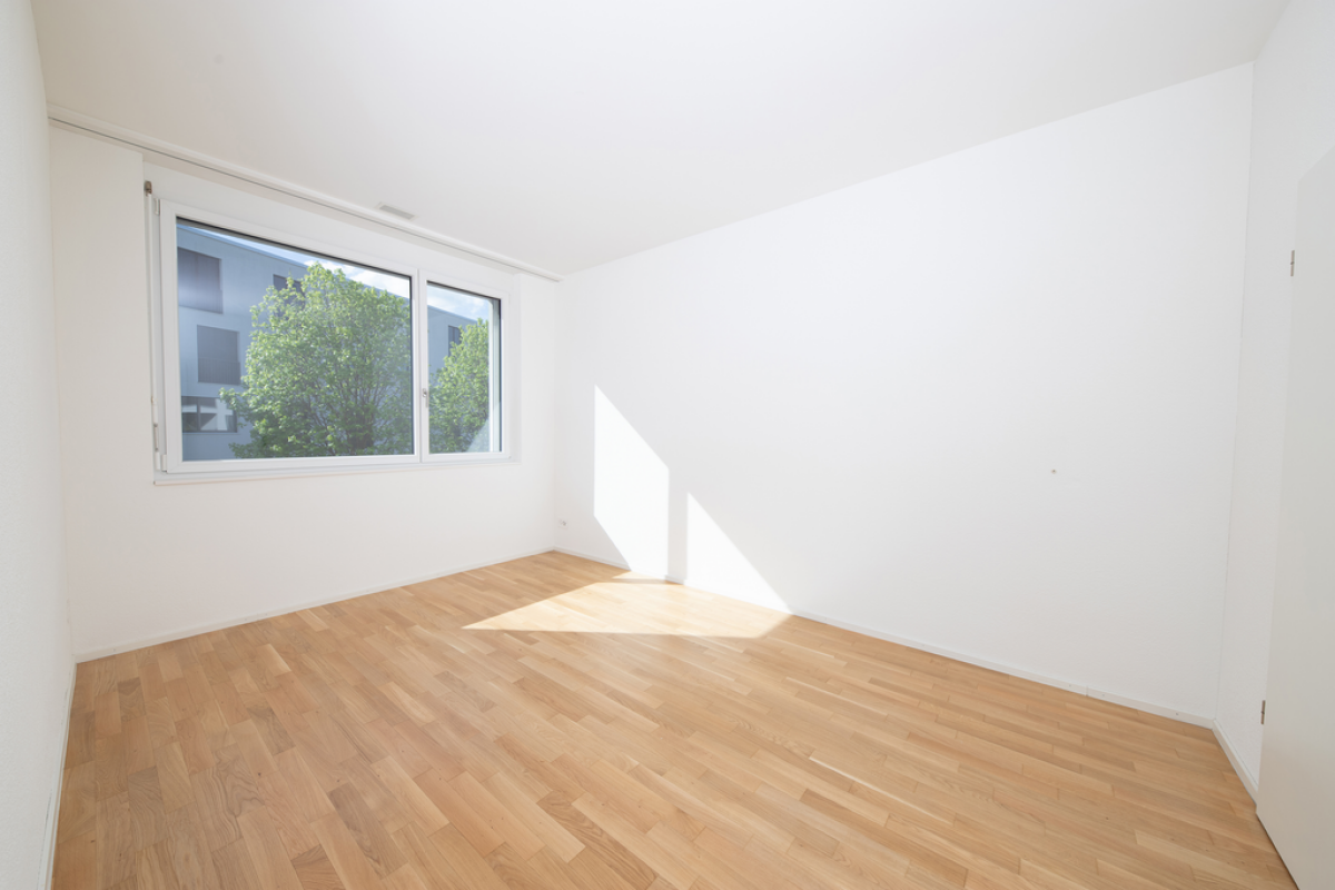 Heller leerer Raum mit Parkett und großem Fenster