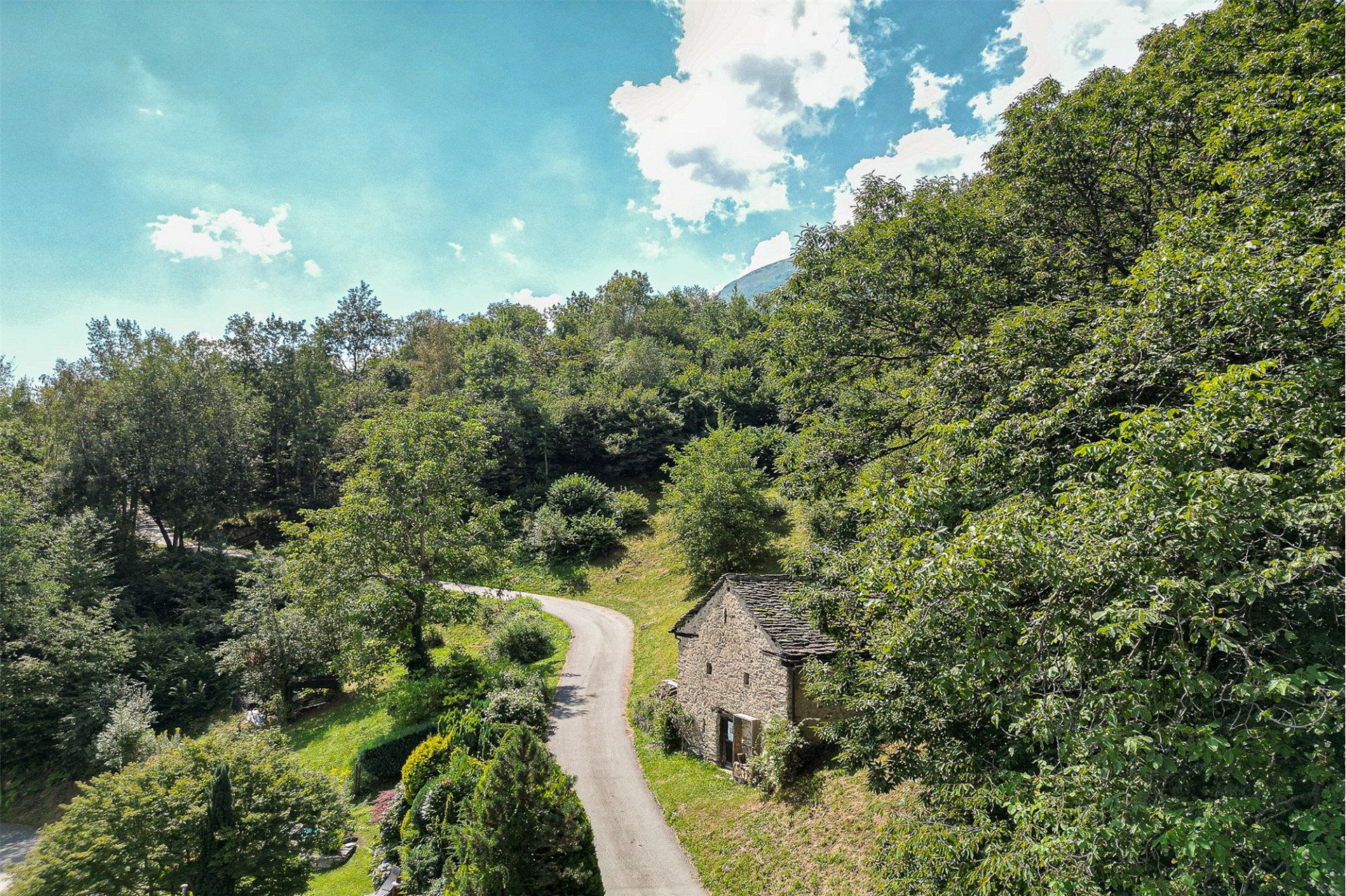 Ländliche Zufahrt mit Steinbau und Waldhang