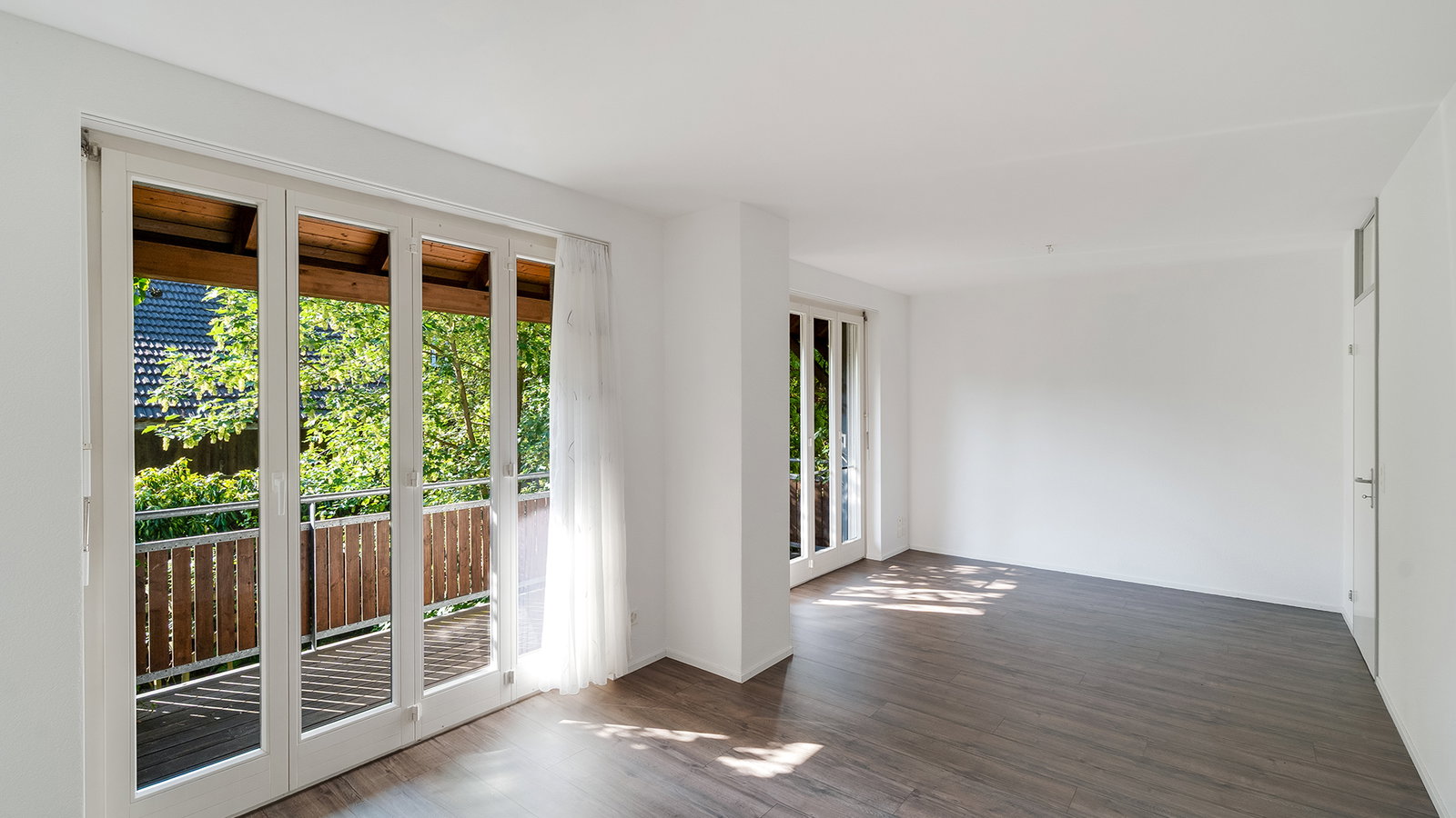 Heller leerer Wohnraum mit Balkon und großen Fenstertüren