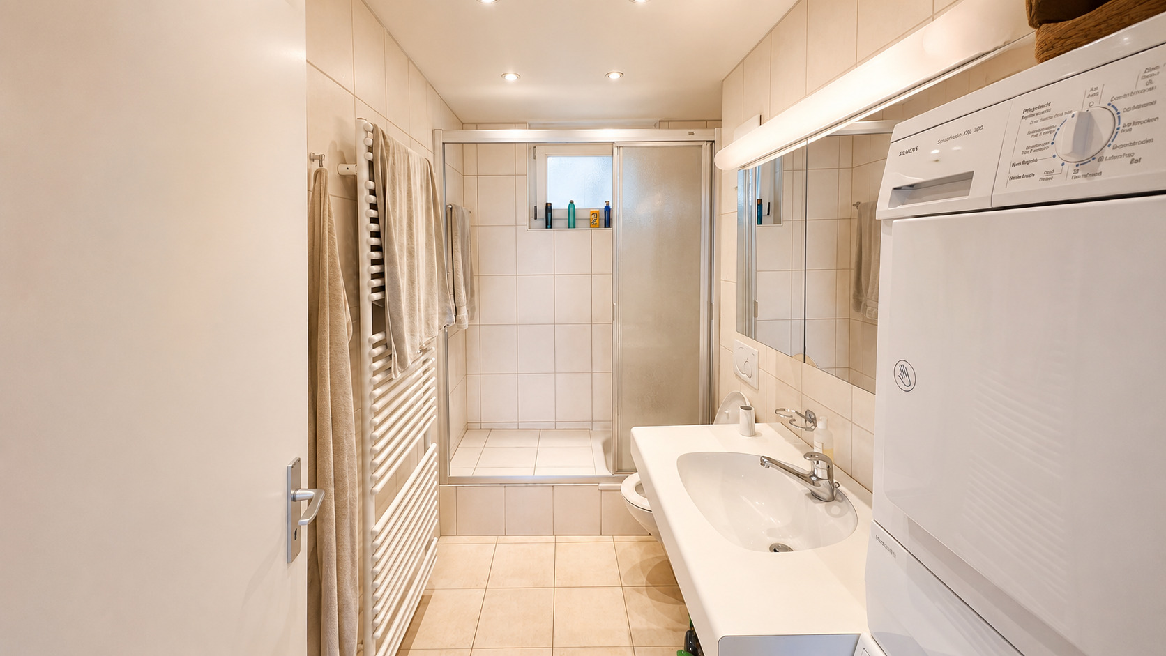 Helles, schmal geschnittenes Badezimmer mit Dusche, Waschtisch und Waschmaschine