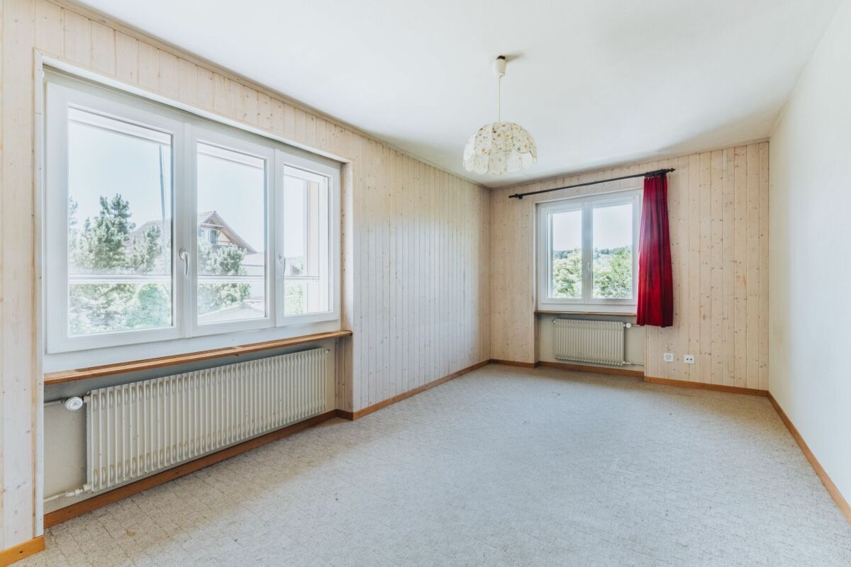 Helles, leeres Zimmer mit Holzpaneelen und zwei Fenstern