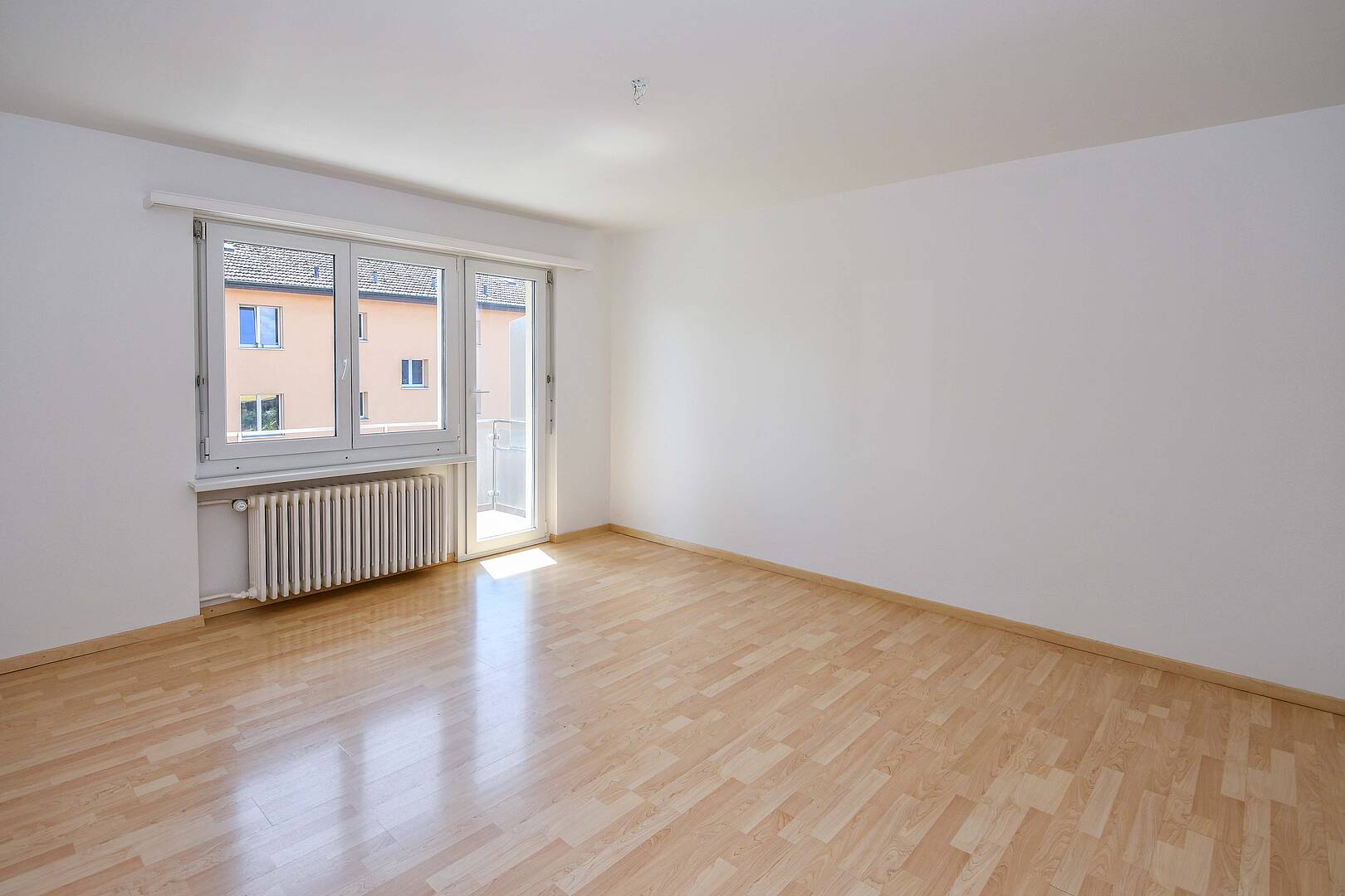 Heller leerer Wohnraum mit Balkon und Blick auf Nachbargebäude
