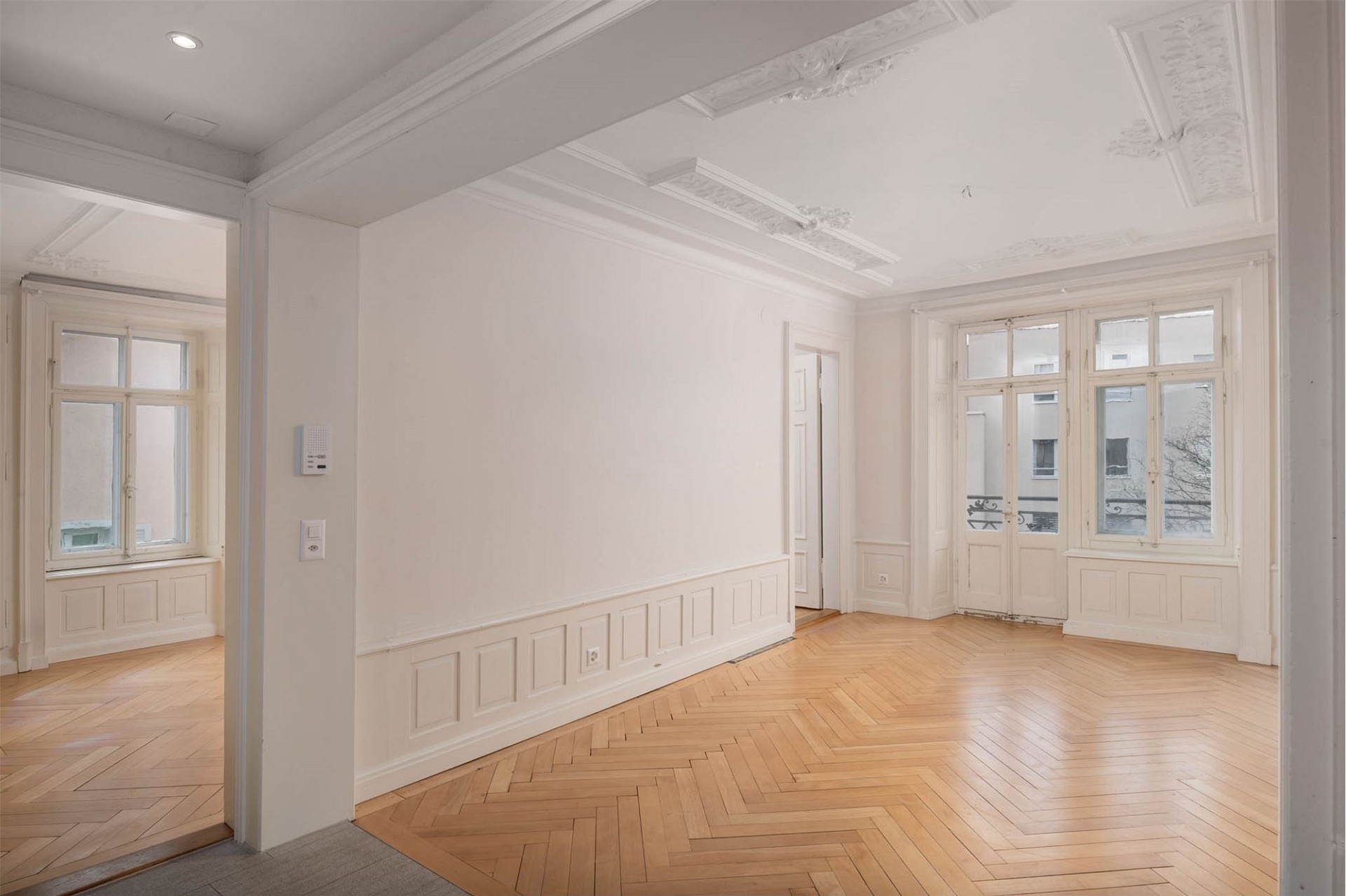 Heller, leerer Altbau-Raum mit Stuckdecken und Fischgrätparkett