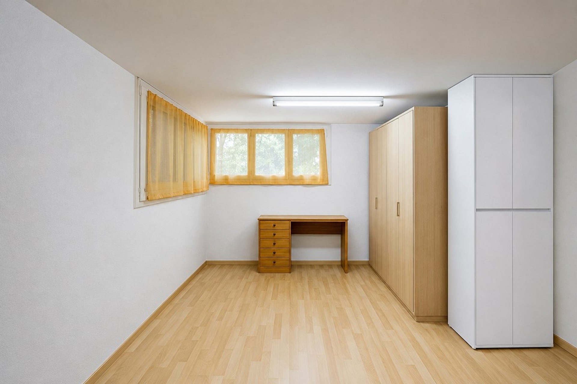 Kleines, schlichtes Zimmer mit Schreibtisch und Schränken