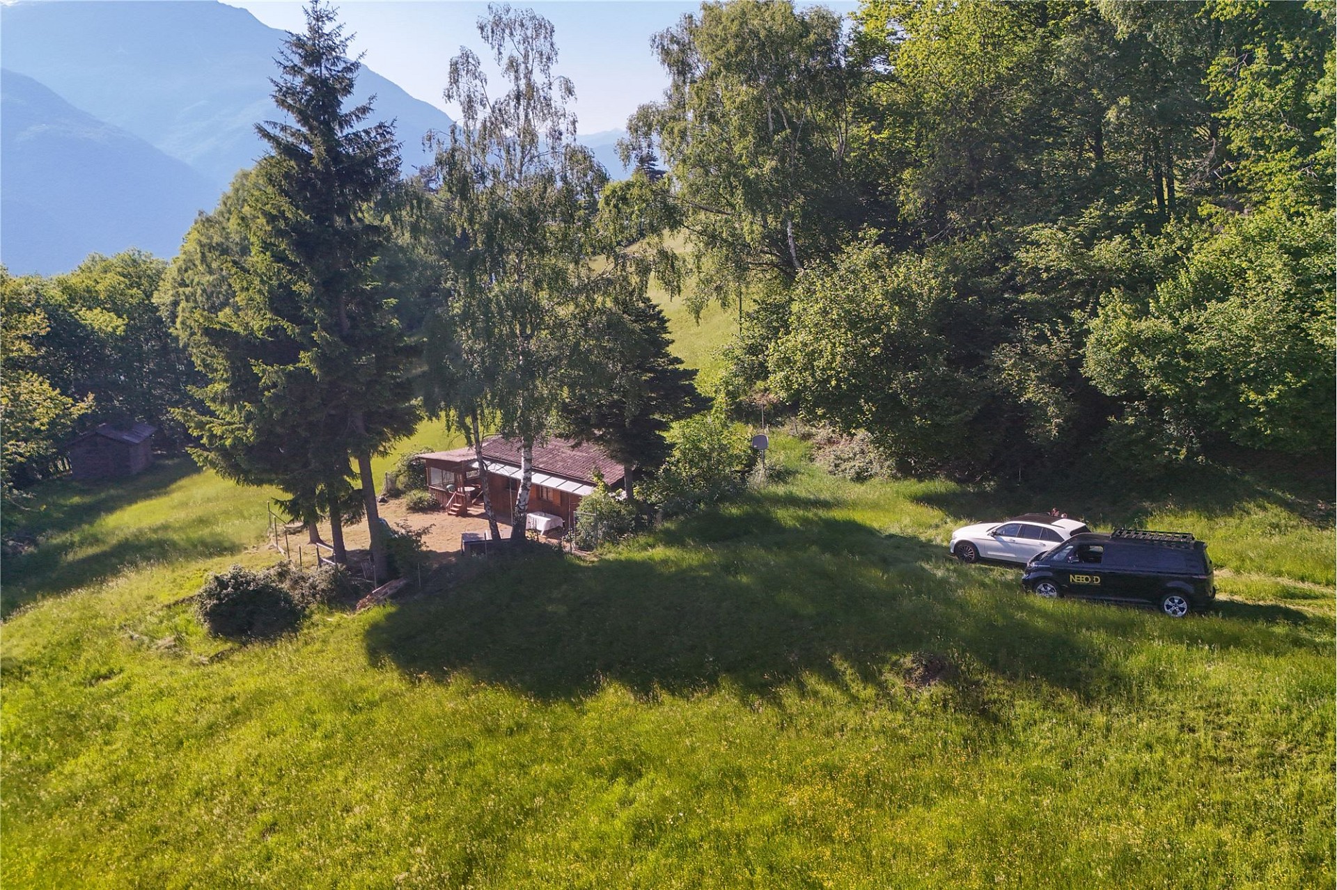 Ländliche Außenansicht mit Wiese, Bäumen und kleinem Gebäude