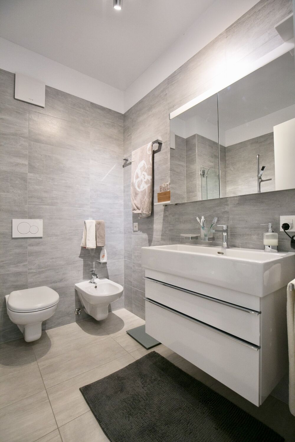 Modernes Badezimmer mit grauen Fliesen und wandhängenden Sanitärobjekten