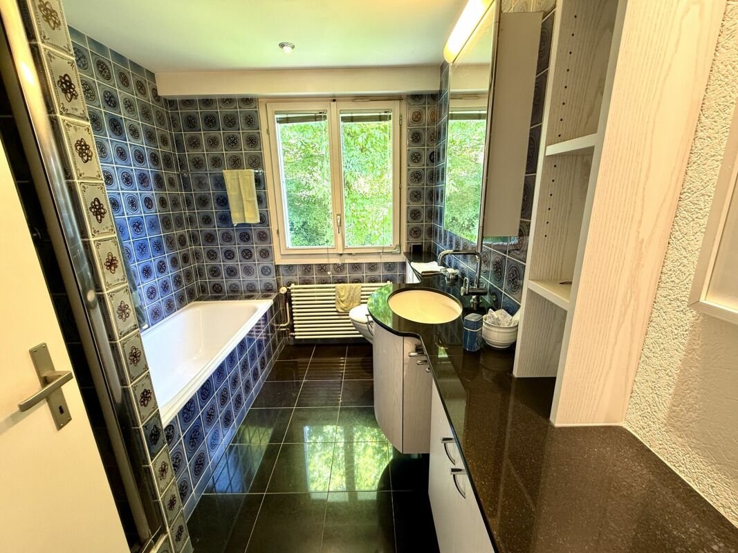 Badezimmer mit blau gemusterten Fliesen und Fensterblick ins Grüne