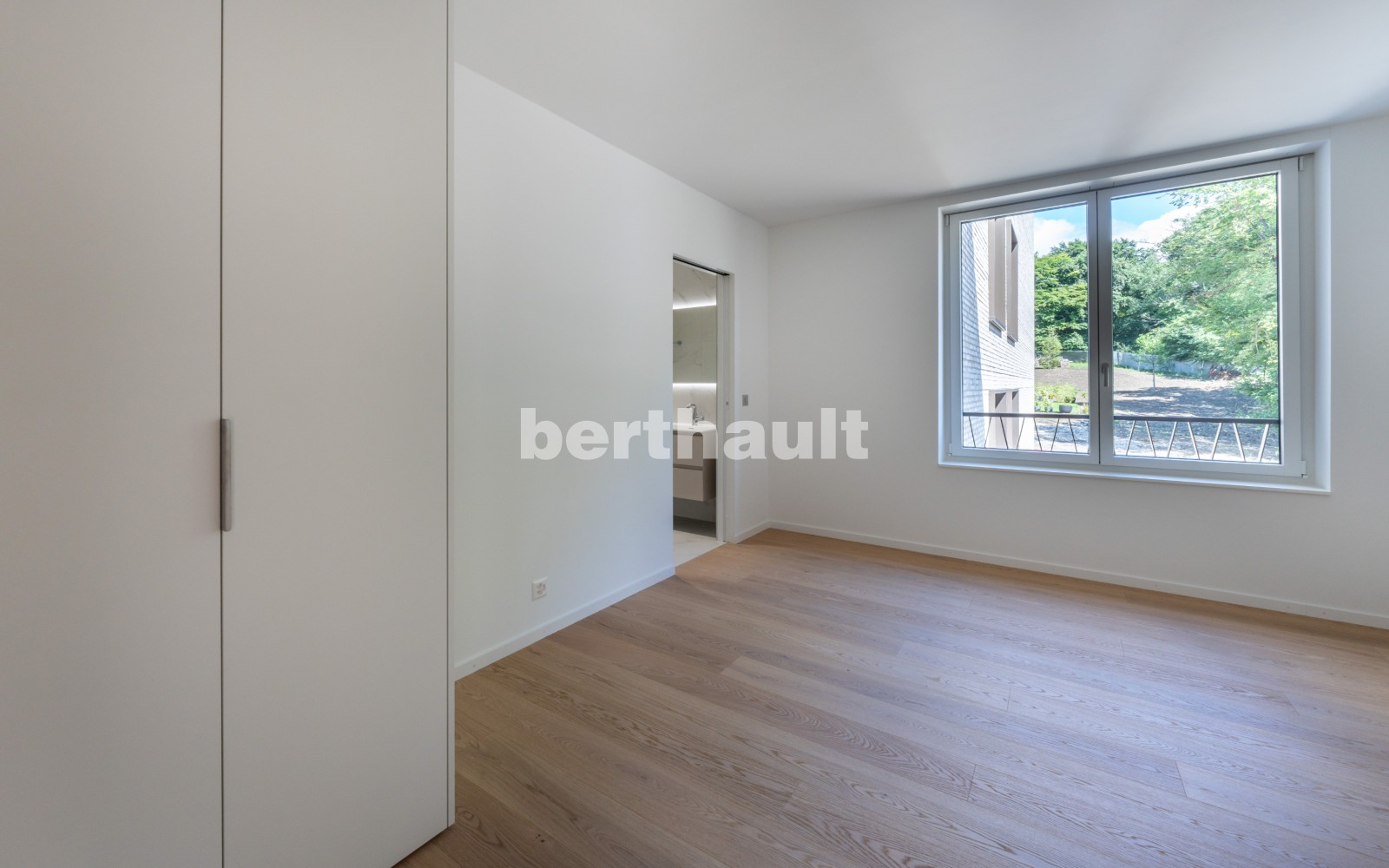 Helles, leeres Schlafzimmer mit Holzboden und großem Fenster