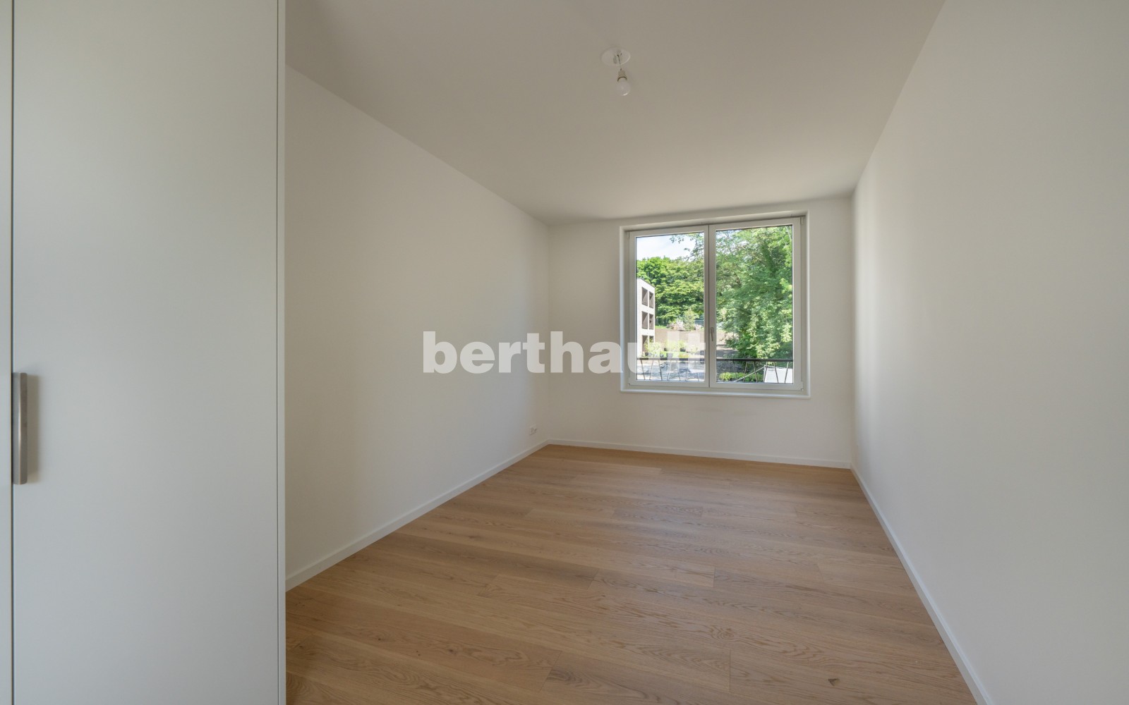 Helles, leeres Schlafzimmer mit Parkett und Fensterblick