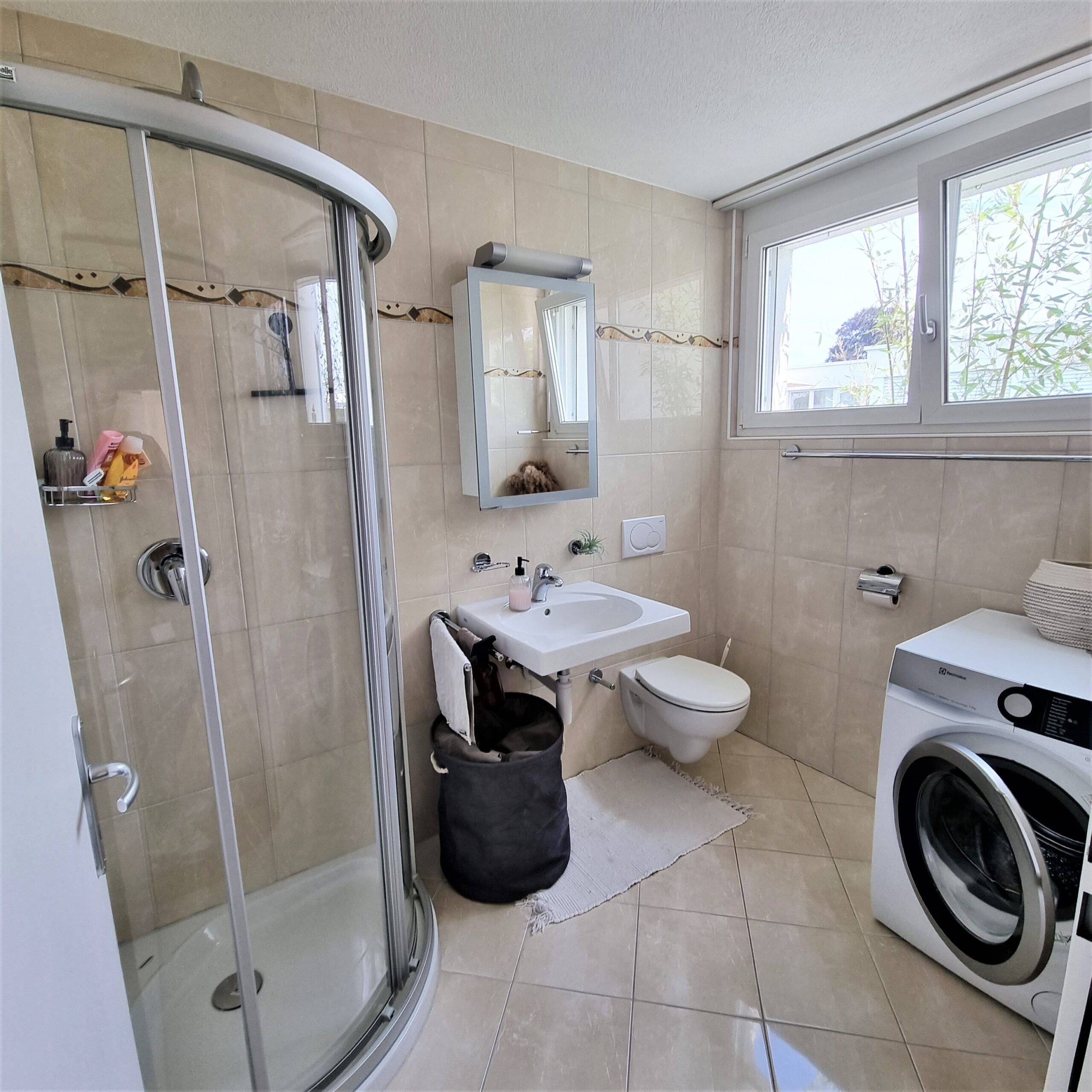 Modernes Badezimmer mit Dusche, WC, Fenster und Waschmaschine