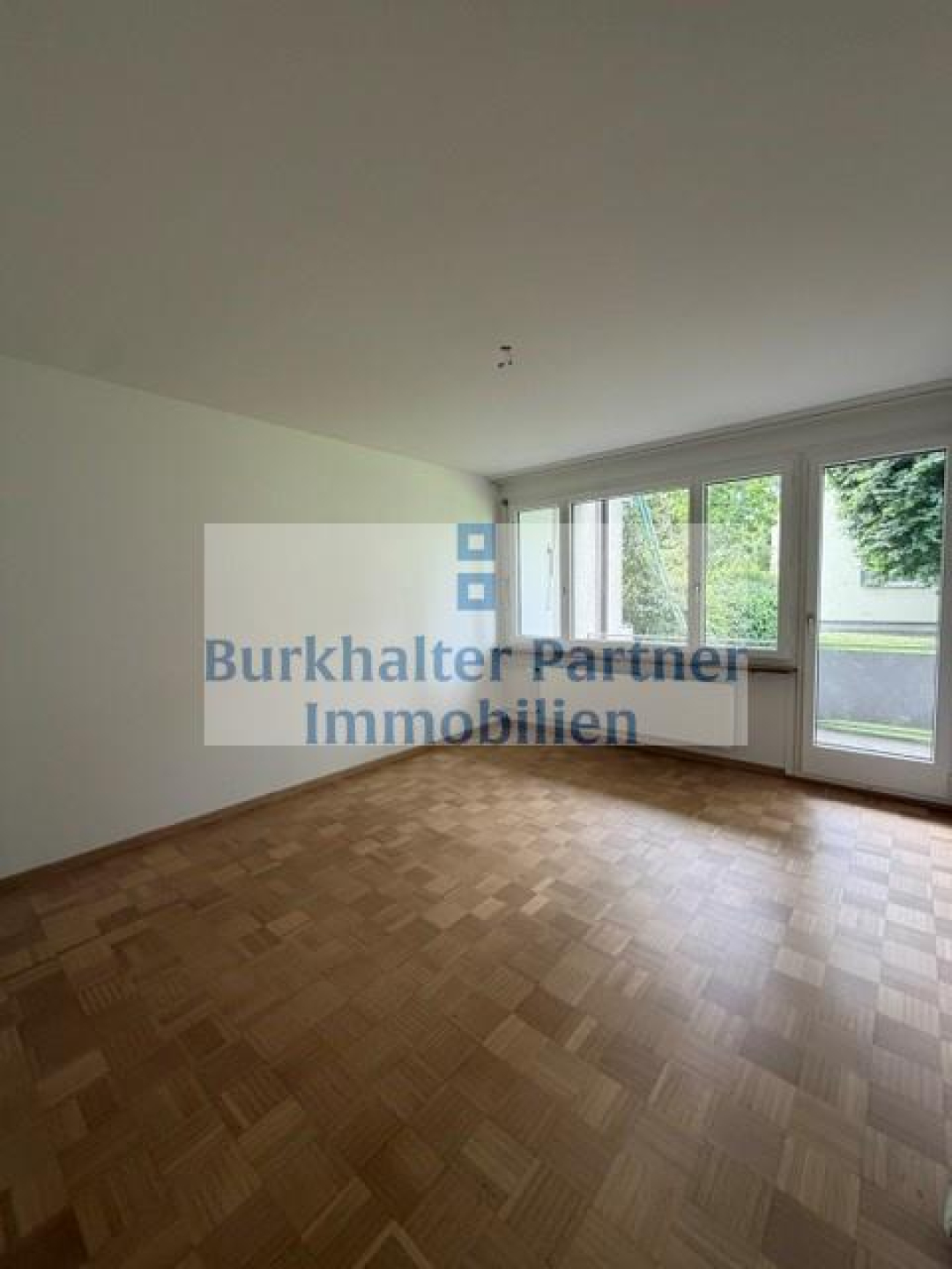 Leerer Wohnraum mit Parkett und Balkon-/Terrassentür