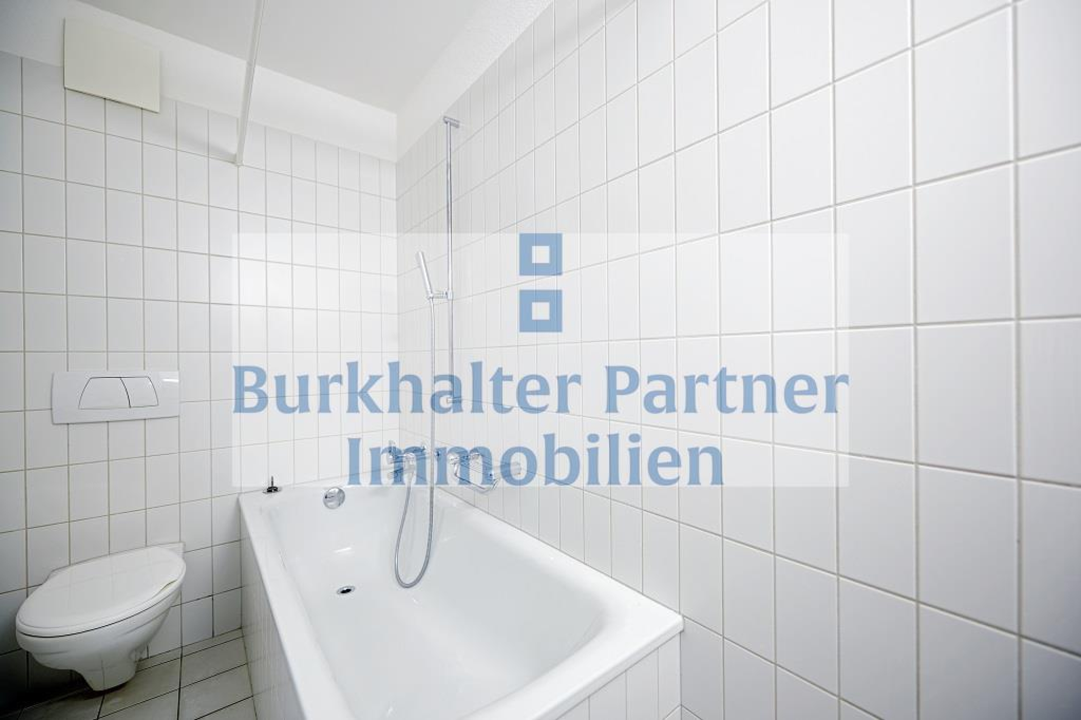 Kleines weiß gefliestes Badezimmer mit Badewanne und WC