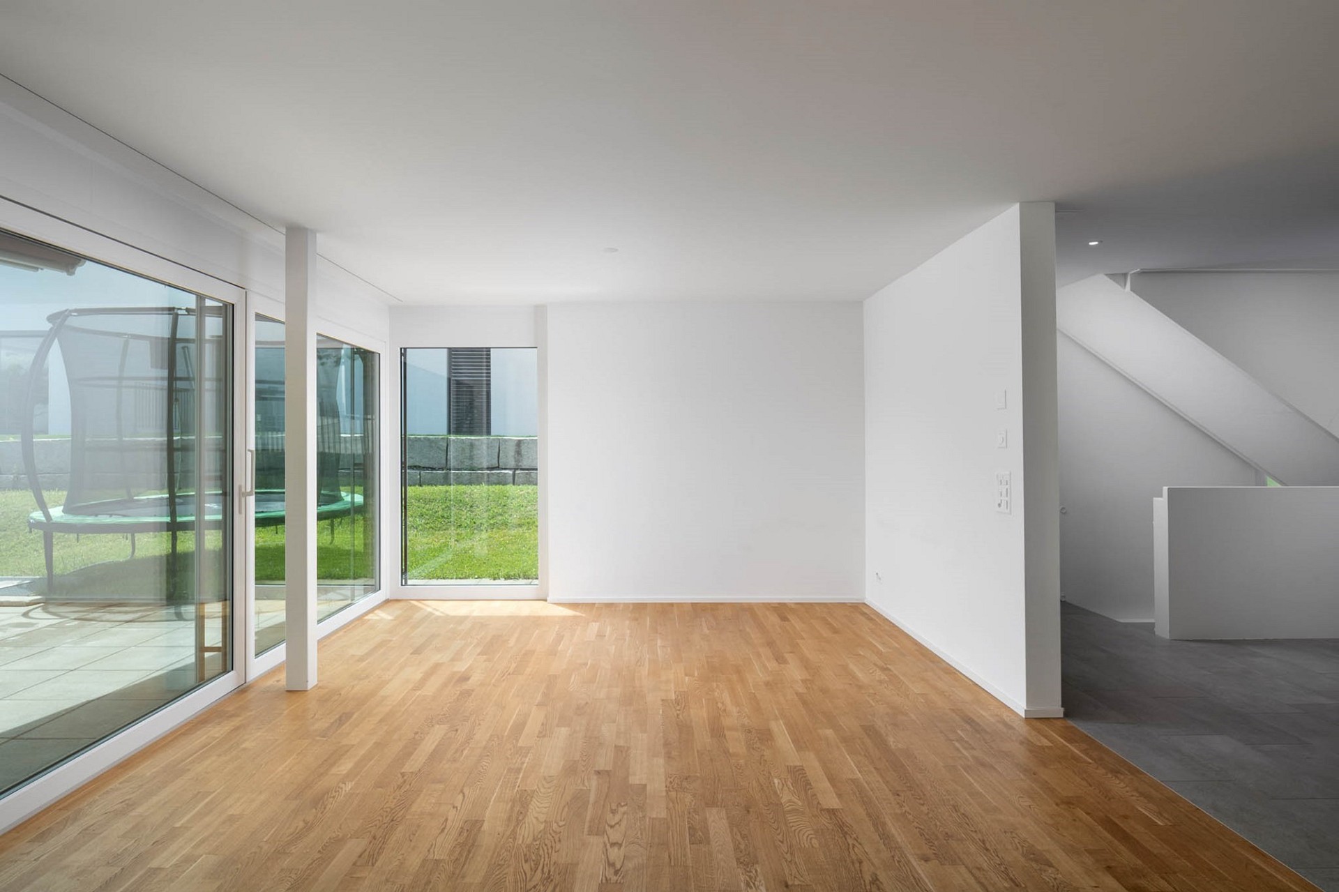 Heller, leerer Wohnraum mit Holzfußboden und großen Fenstern