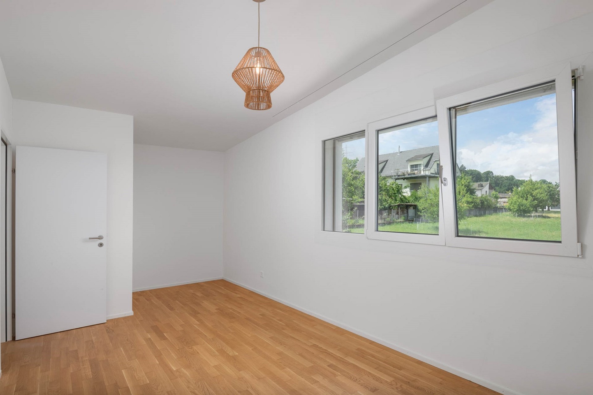 Helles, leeres Zimmer mit Fensterfront und Holzpendelleuchte