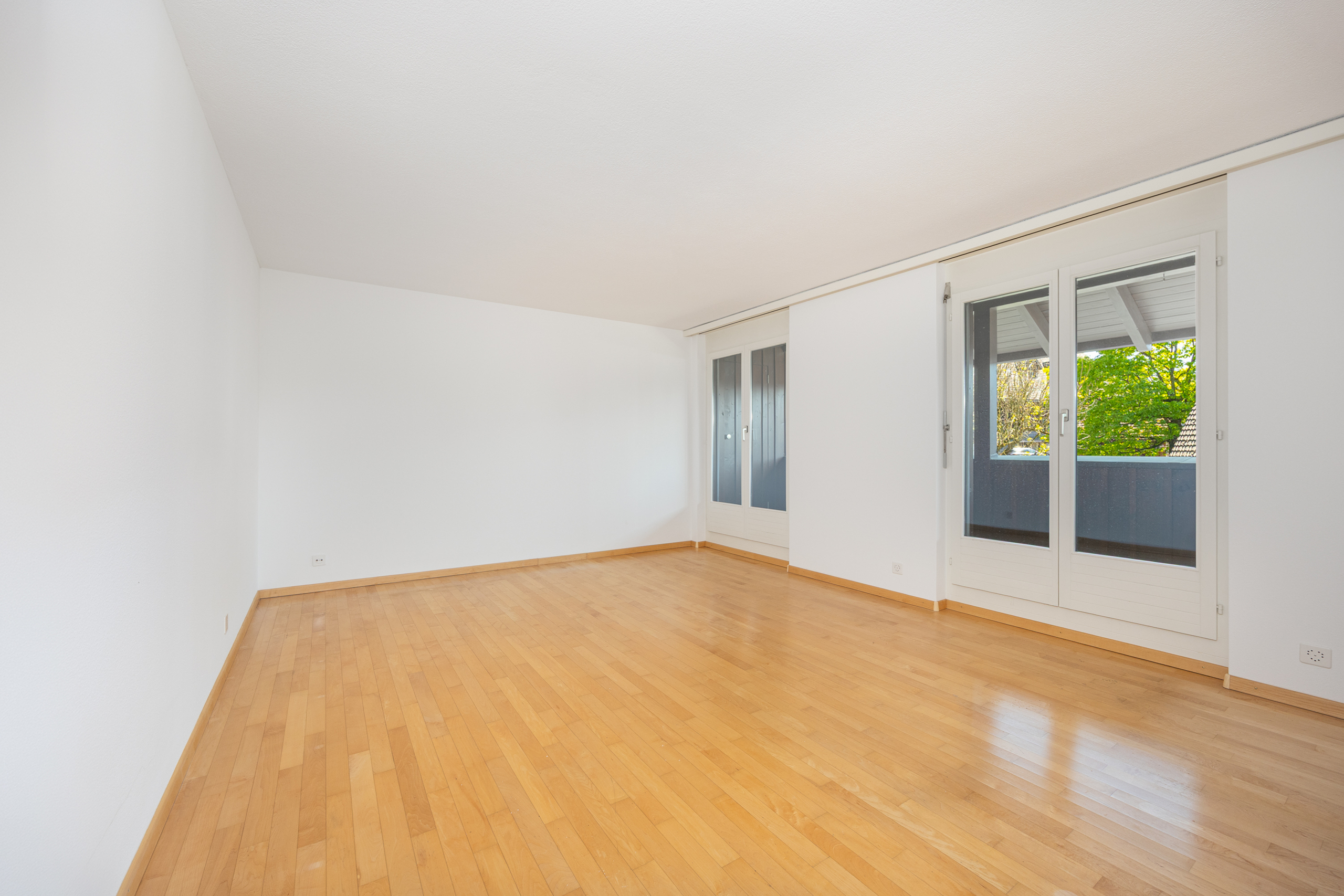 Leerer heller Wohnraum mit Parkett und Balkon-/Fenstertüren