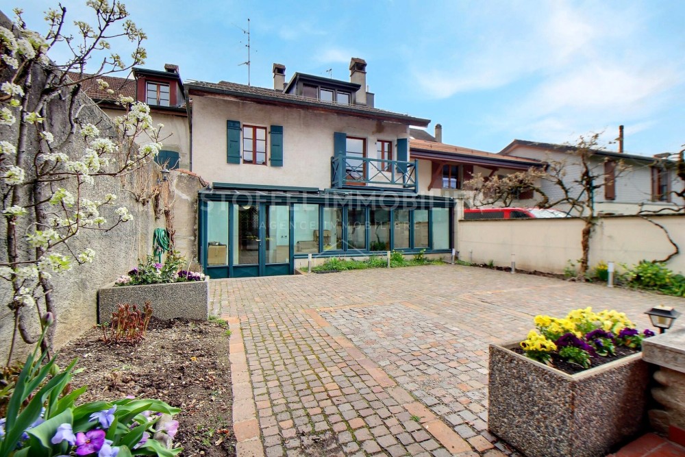 Außenansicht eines Wohnhauses mit gepflastertem Hof und Gartenbeeten