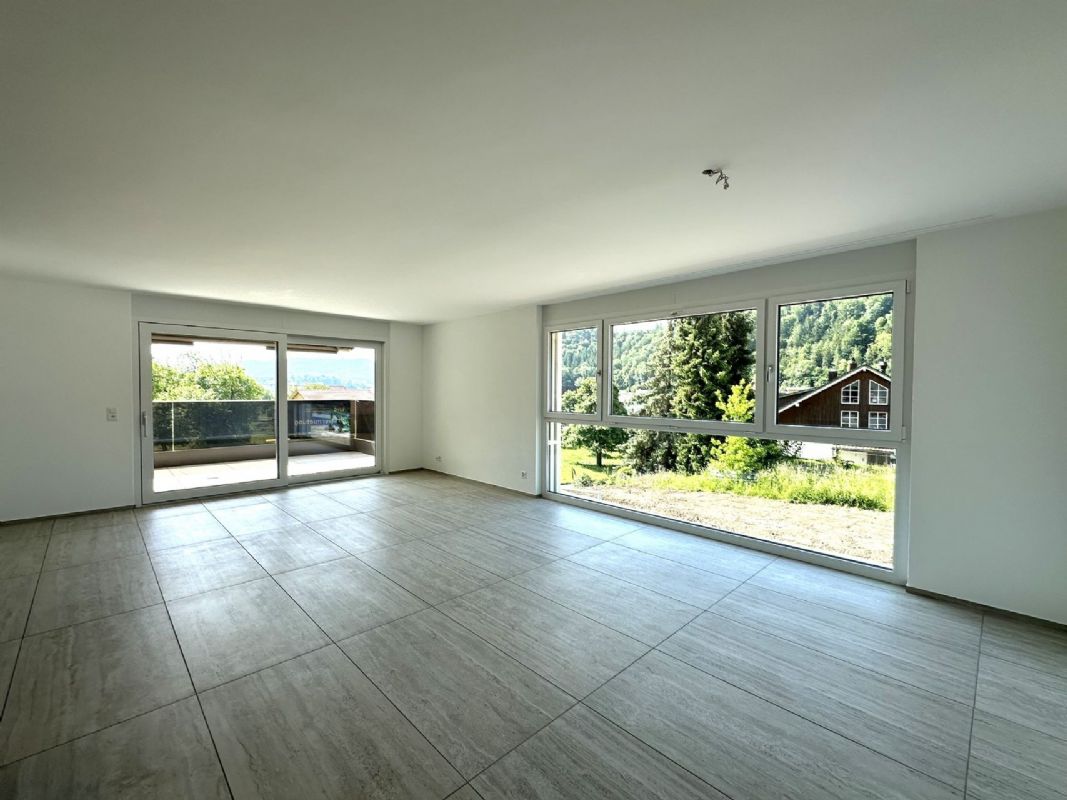 Leerer, heller Wohnraum mit großen Fensterfronten und Balkon